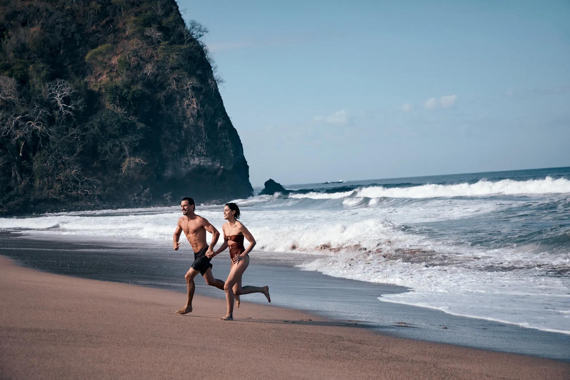 Couple holding hands running on the beach with the mountain as background.