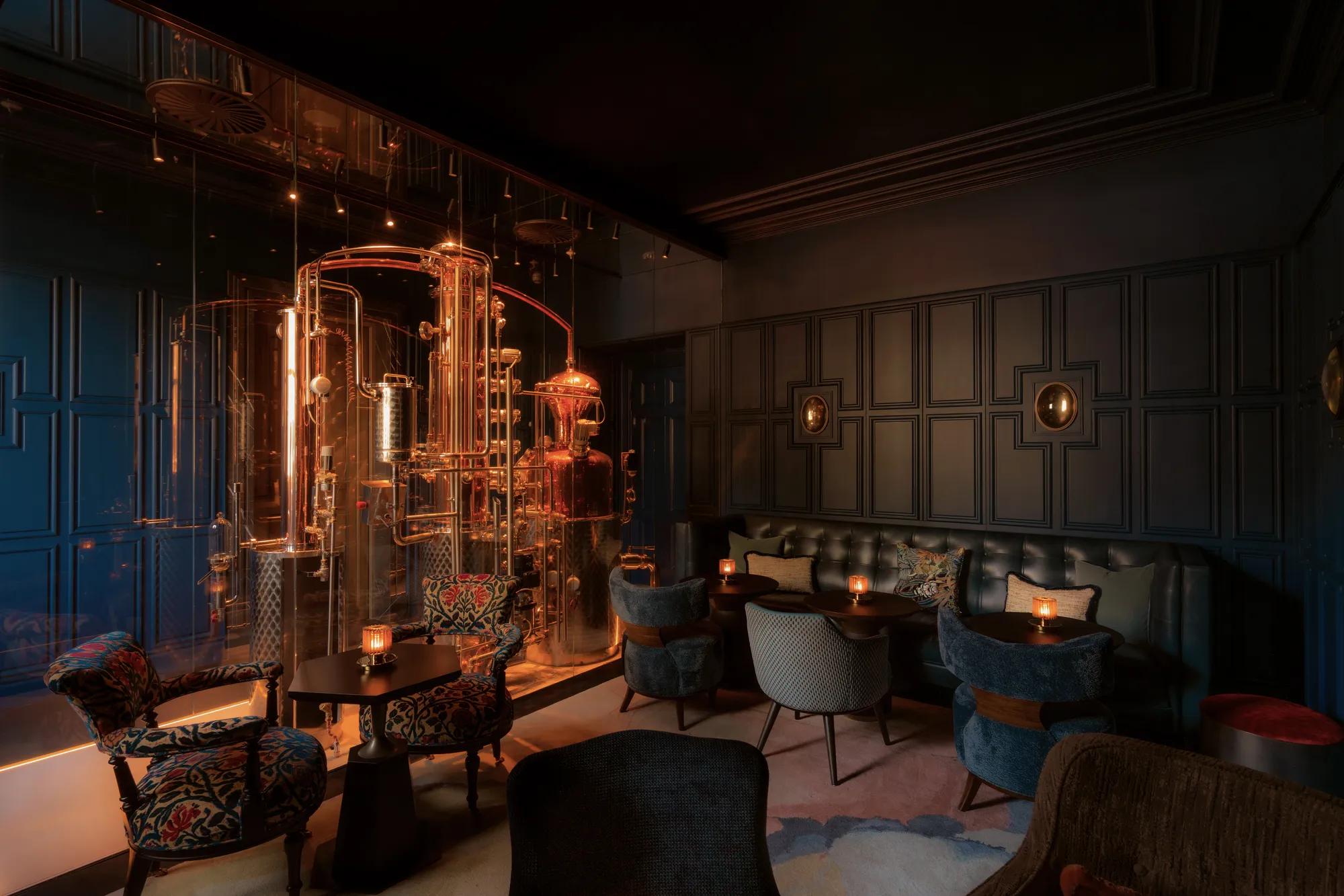 "Lounge bar with dark walls, copper distillery,  and plush seating with candles."