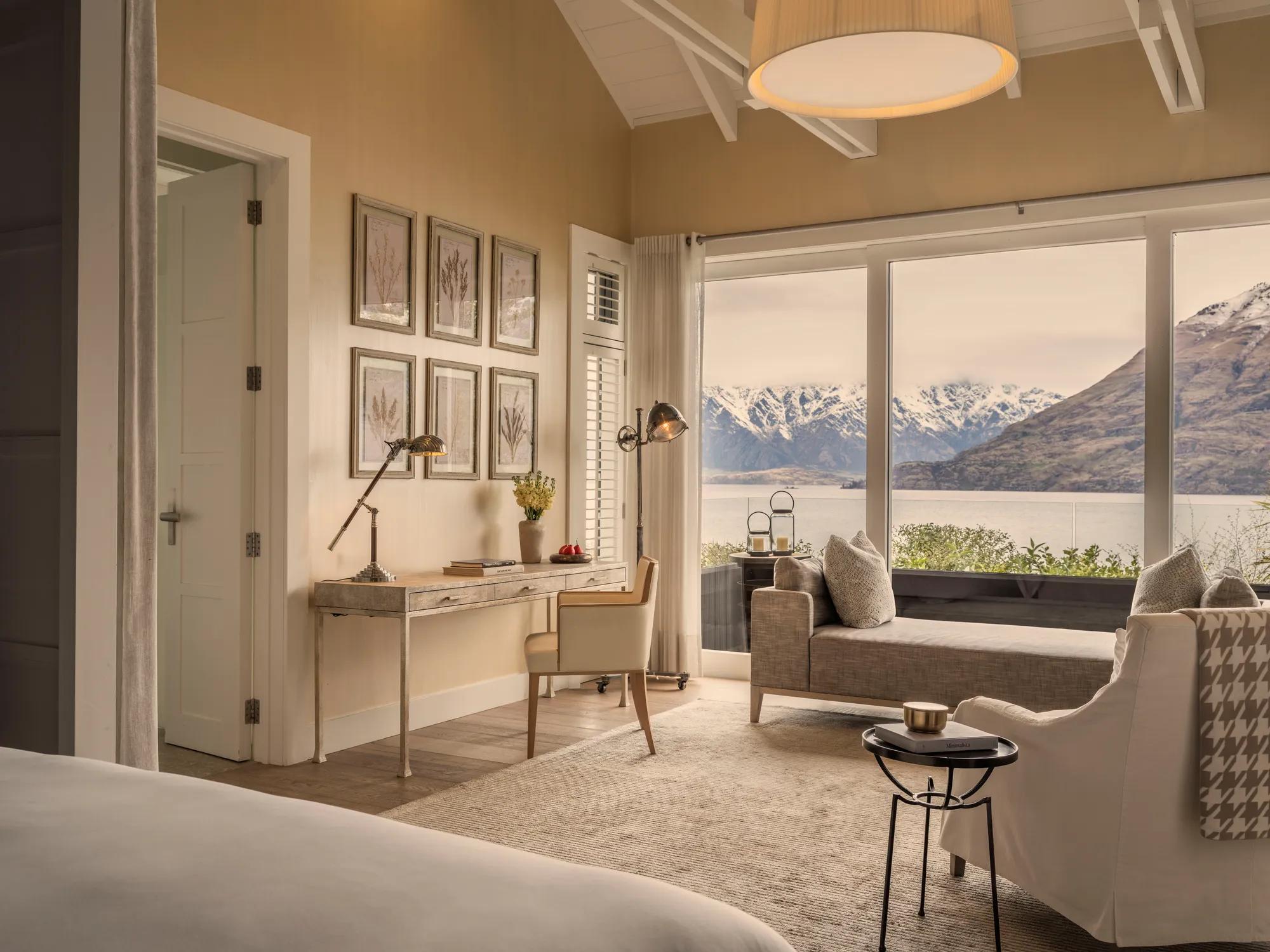 Luxurious hotel suite with plush bedding, desk, armchair, daybed and private balcony with lake and mountain views.