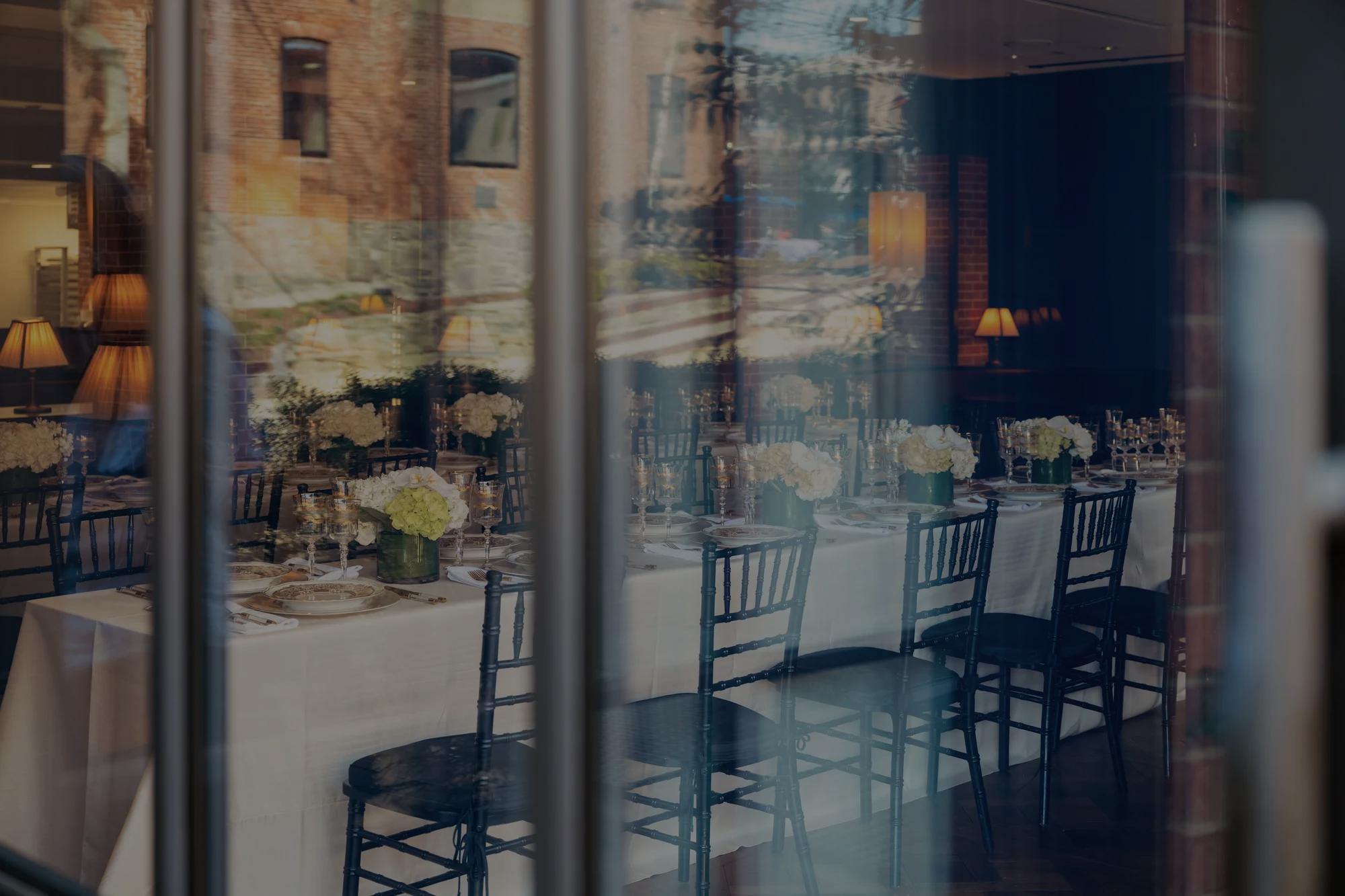 Looking through patio doors at a set long table for a private event with florals and unique place settings.