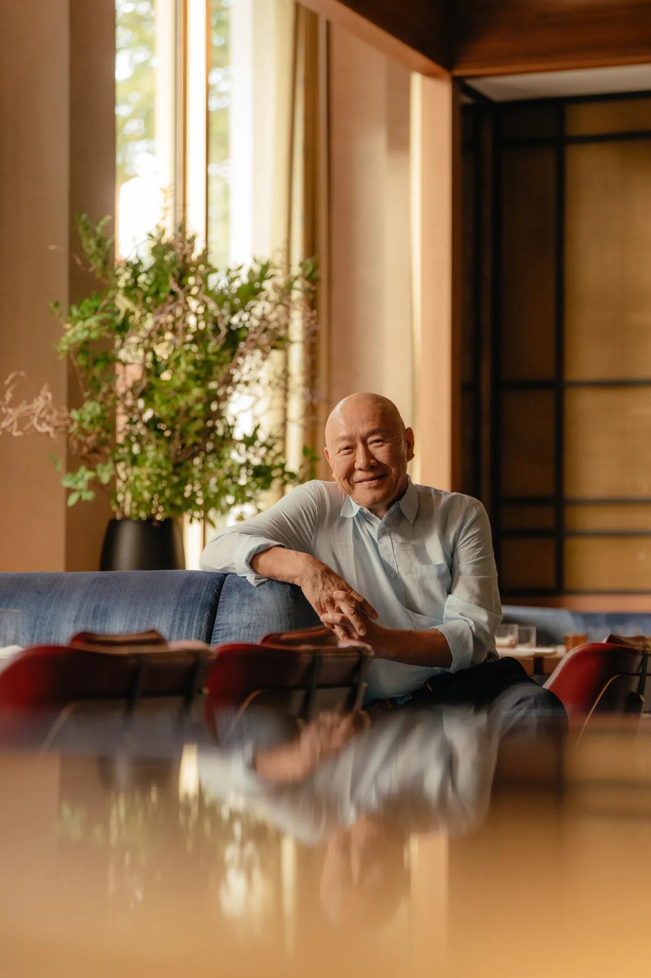 portrait of chef masayoshi takayama sat on deep blue sofas within tobi masa restaurant