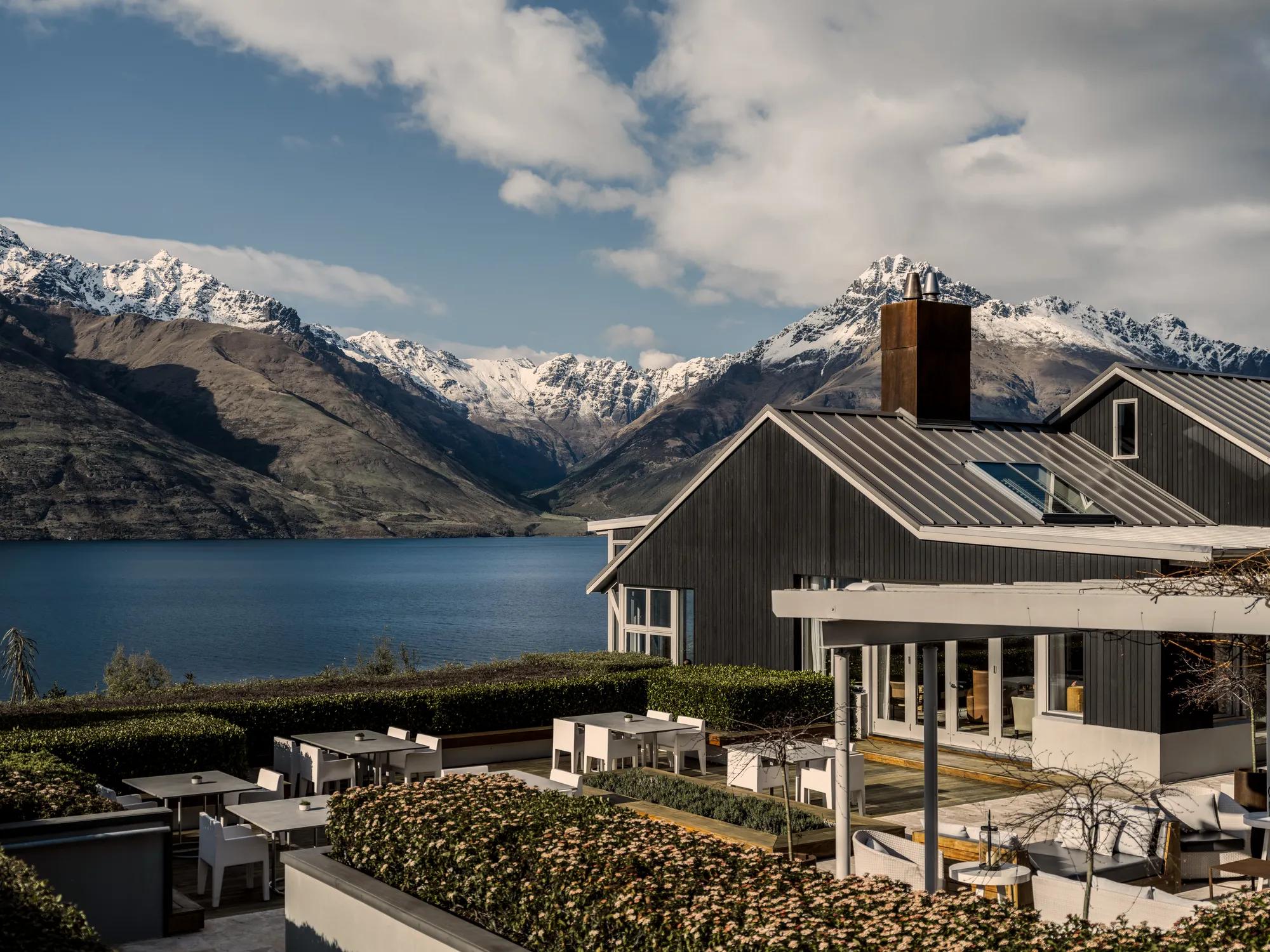 Exterior shot of the main lodge and Remarkables Terrace at Rosewood Matakauri, sitting on the edge of Lake Wakatipu surrounded by snowcapped mountains.