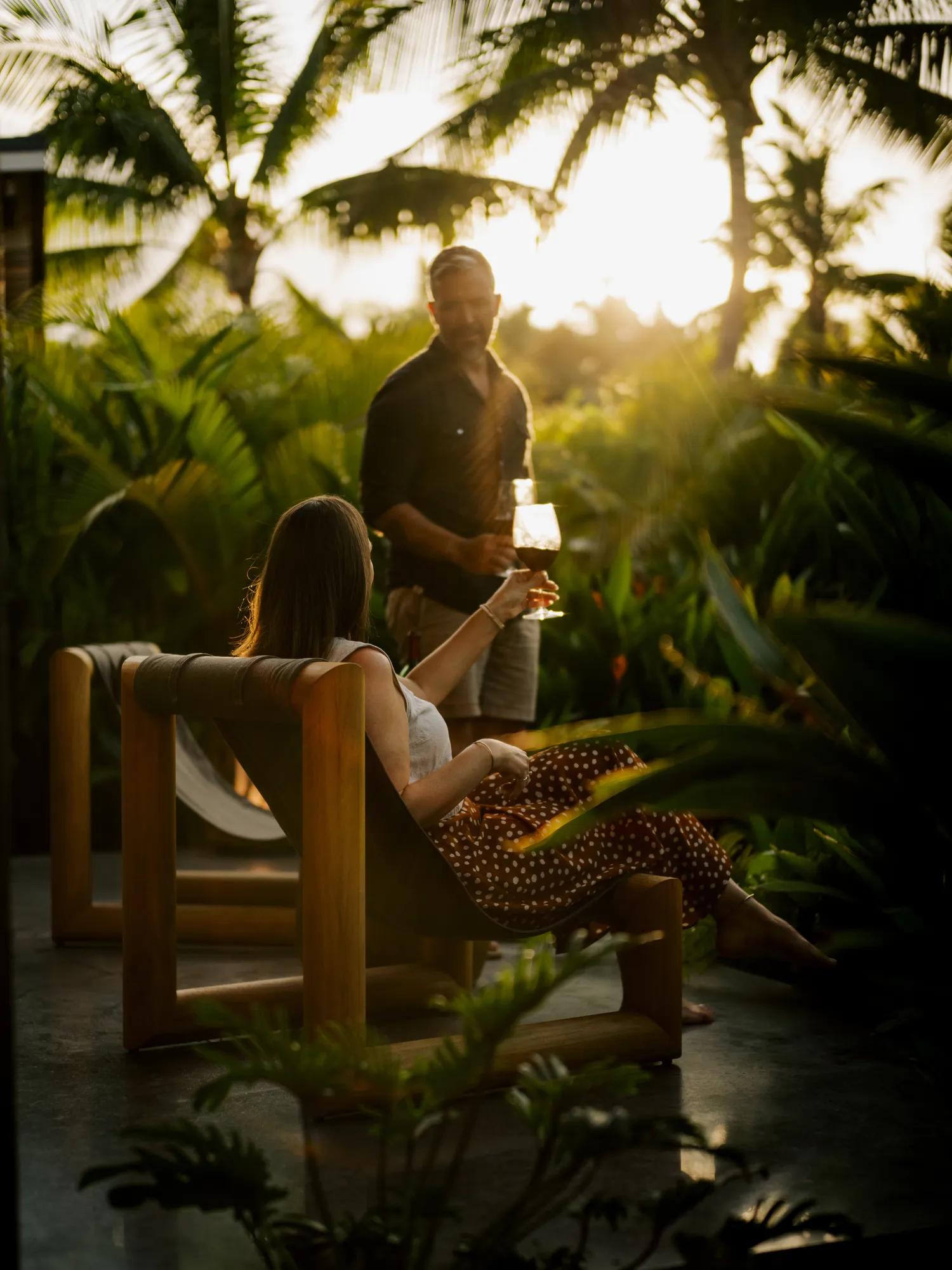 Person holding a orange cocktail garnished with a flower with the beach in the background