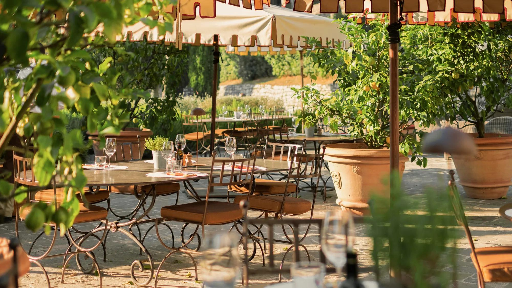 Outdoor dining area with a table set for four under a lemon tree with stone walls in the background.