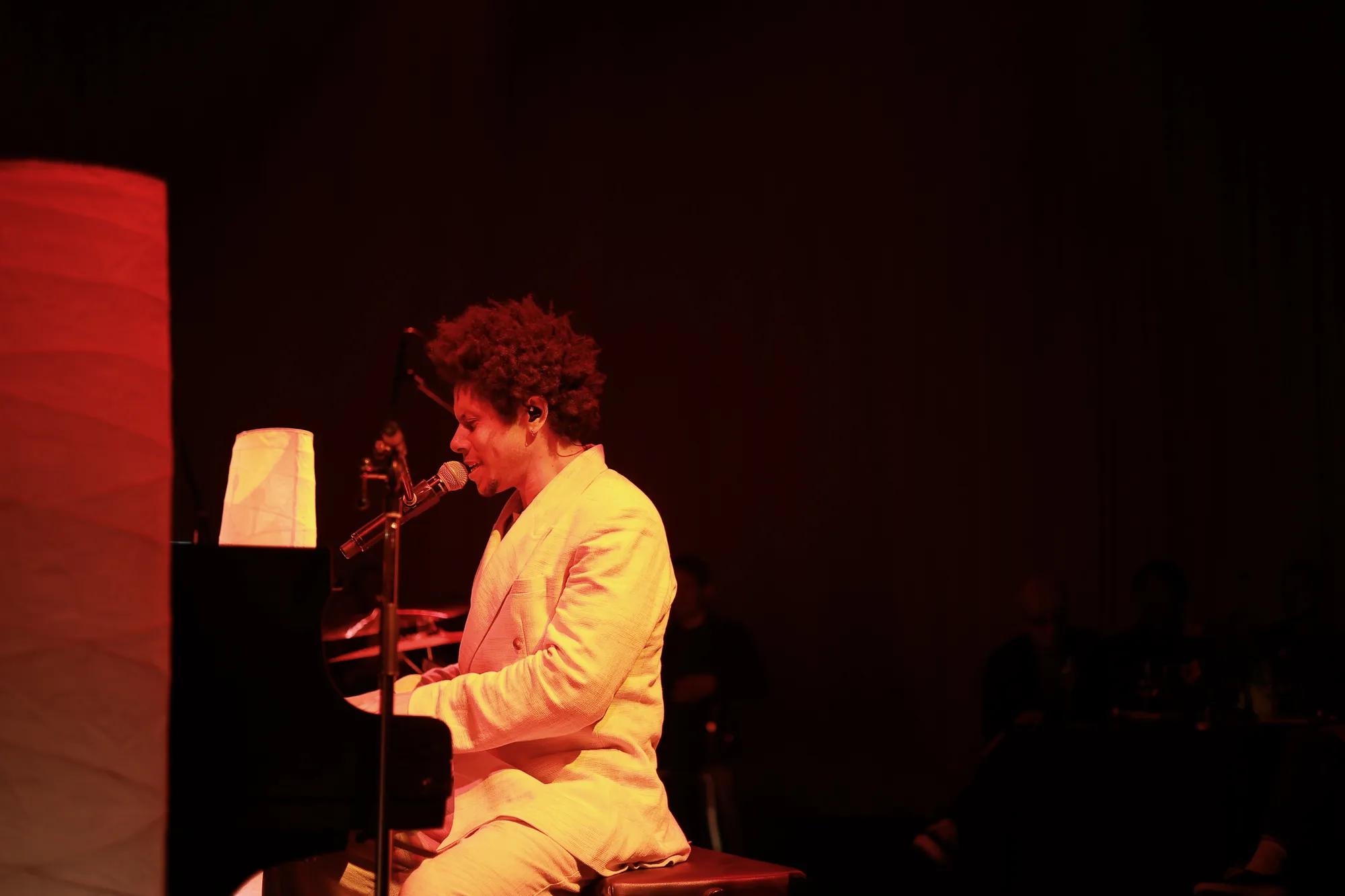 Musician at a piano singing into a microphone with ambient lighting 