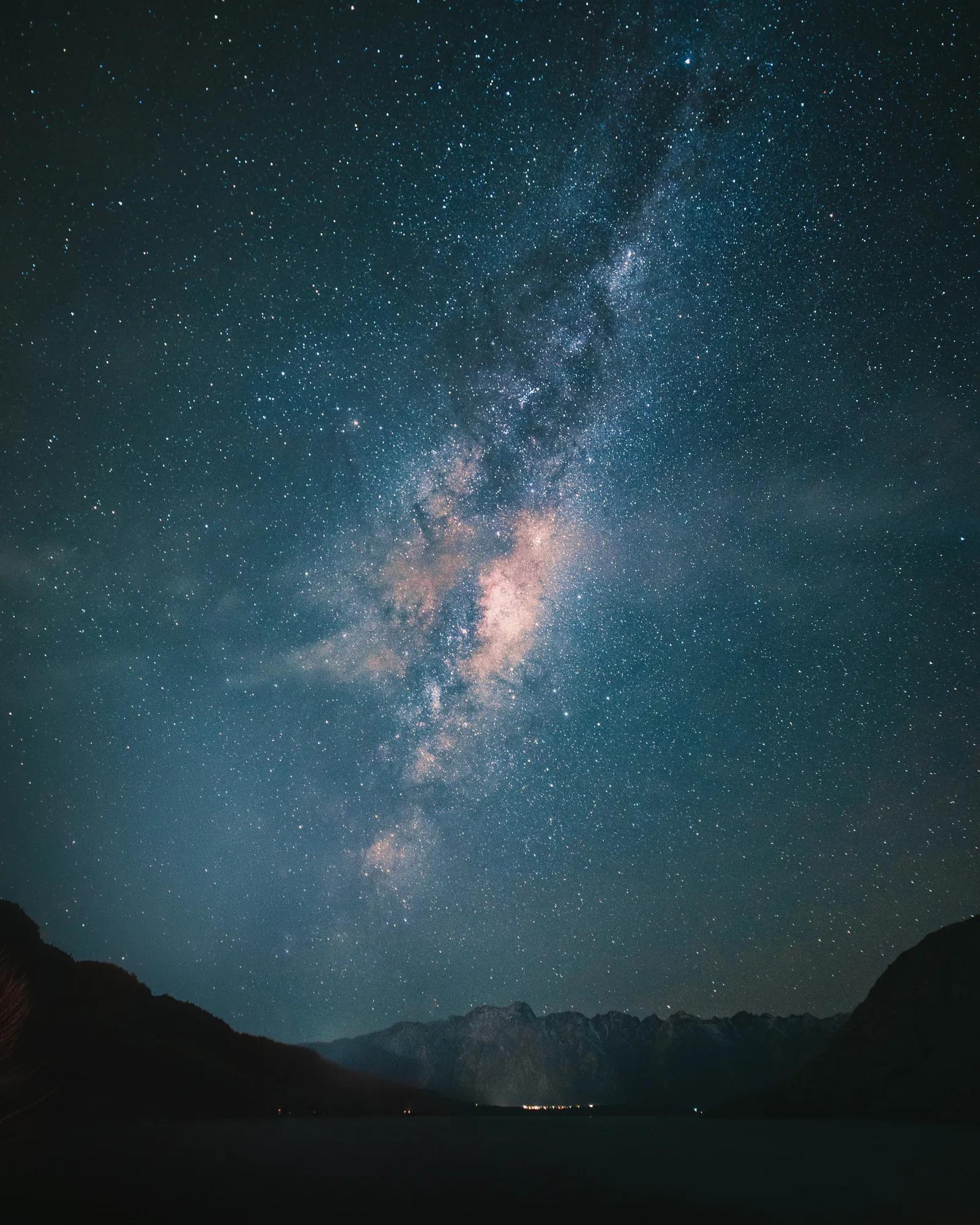 A night time shot of the Remarkables mountain range dimly lit against the background of the milky way core. 