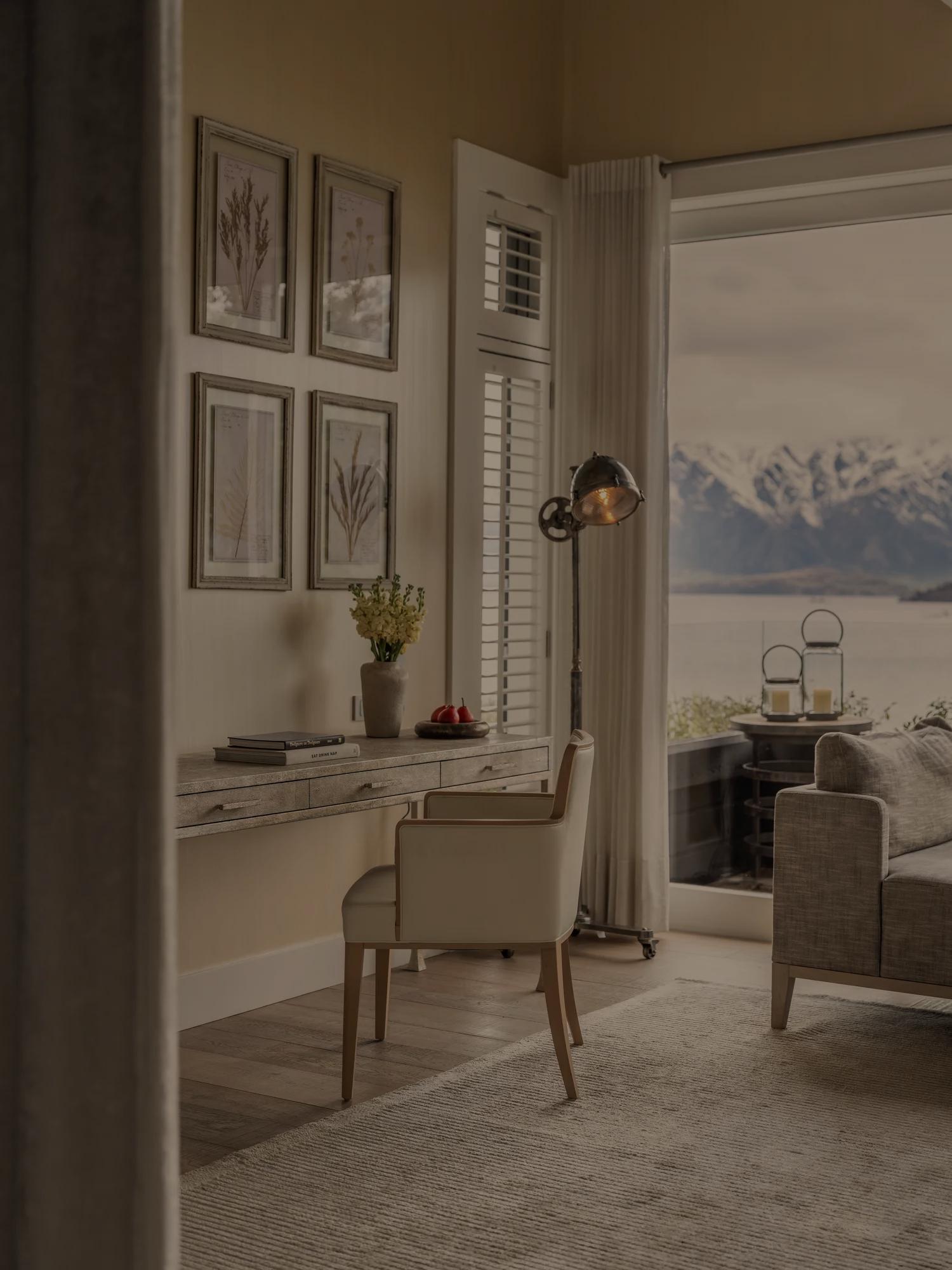 Glimpse into the living area of a luxurious suite with desk, daybed and private balcony with lake and mountain views.