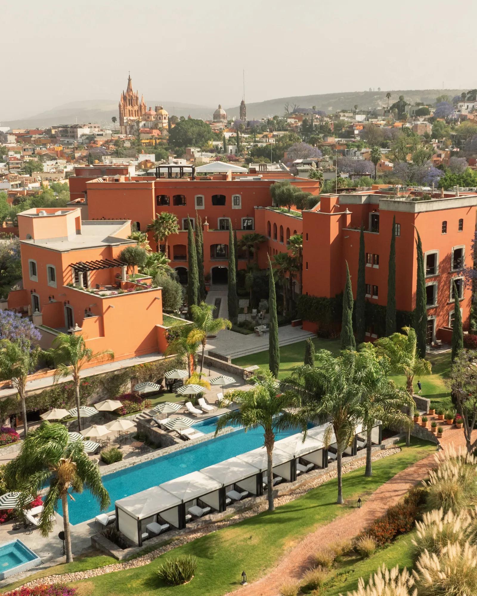 Aerial view of the hotel and pool area with the Parroquia de San Miguel de Allende visible in the background. 