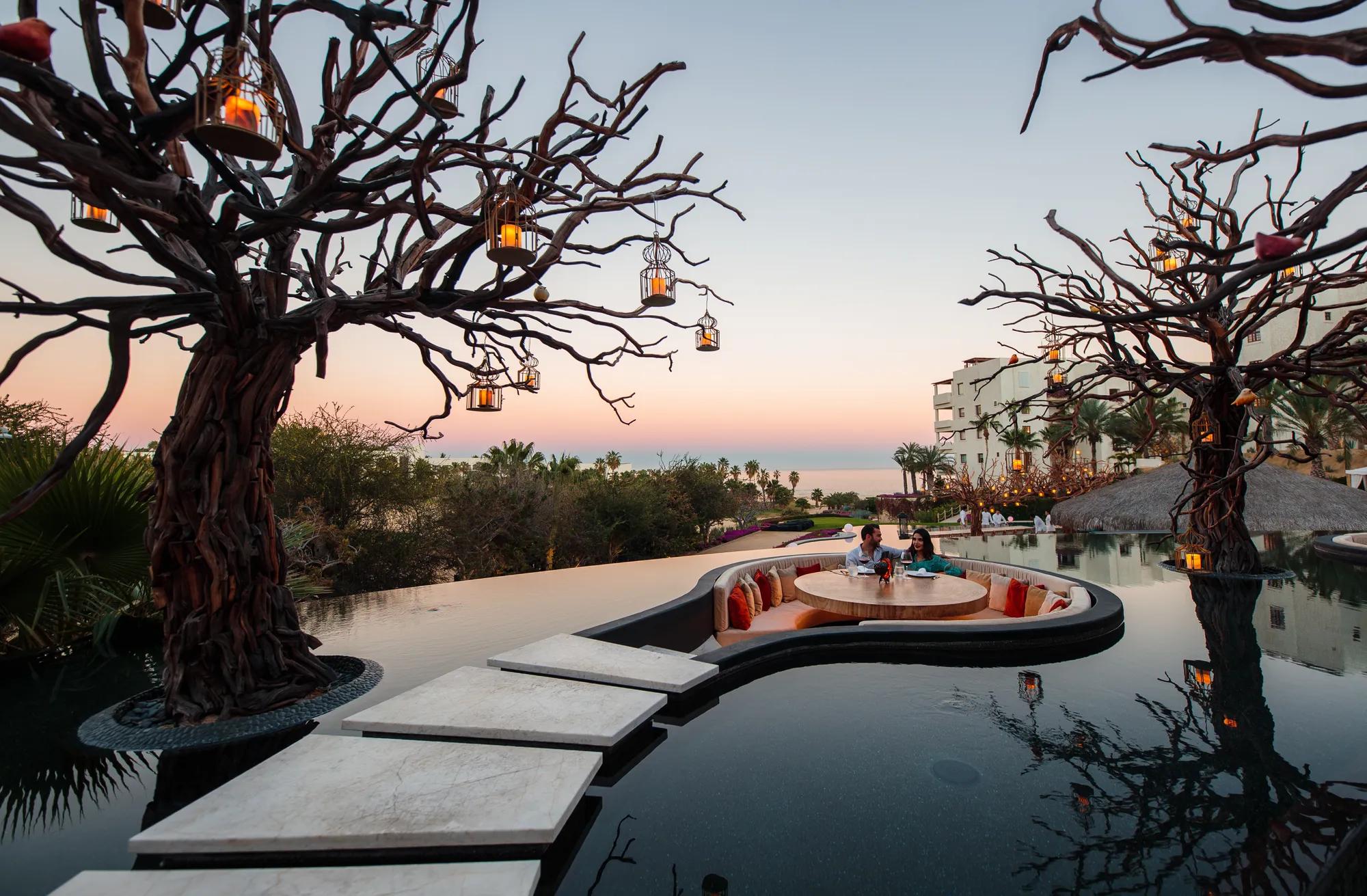 Beachfront resort with thatched-roof structures, an infinity pool, and lounge chairs overlooking the ocean under a clear blue sky