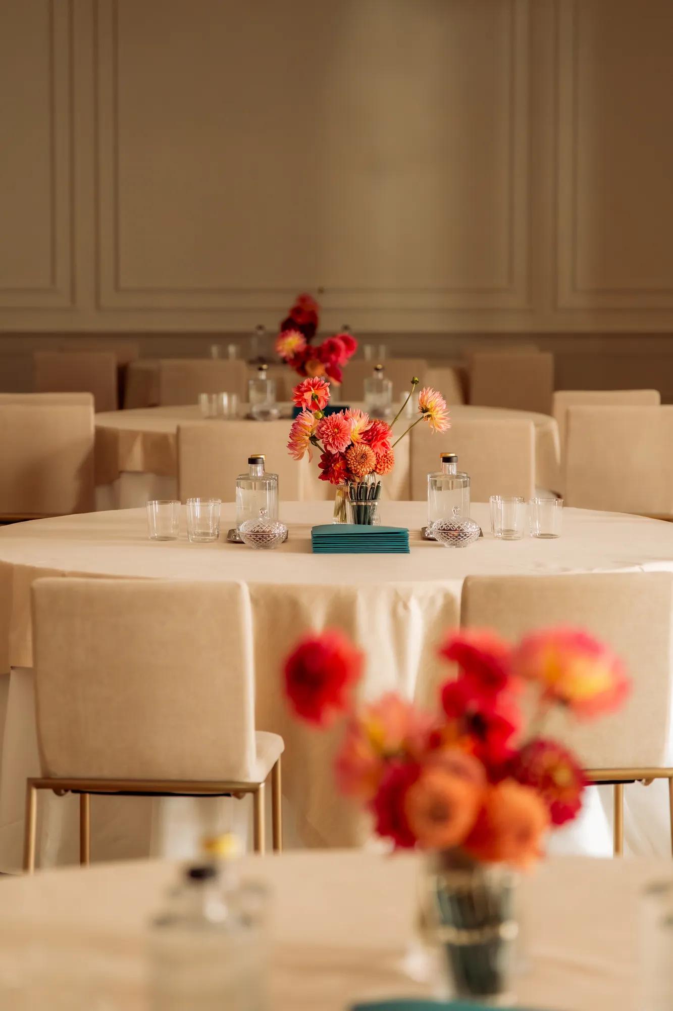 Banquet tables draped in linen decorated with glassware and a vase of flowers 