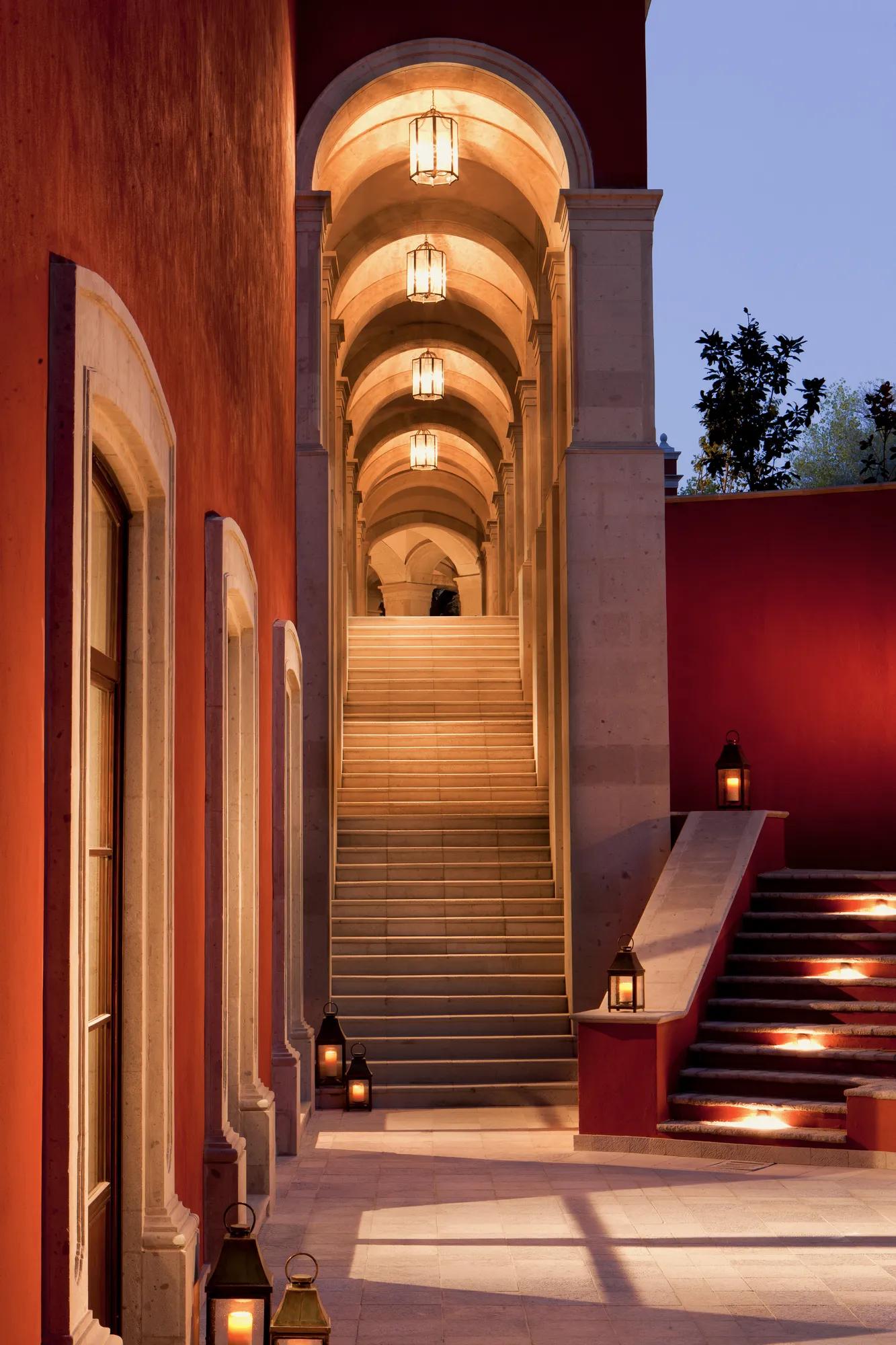 Amphitheater with arched ceiling and hanging lights, viewed from the lower level. A wall with windows appears on the left, opening to a semi-open outdoor space.