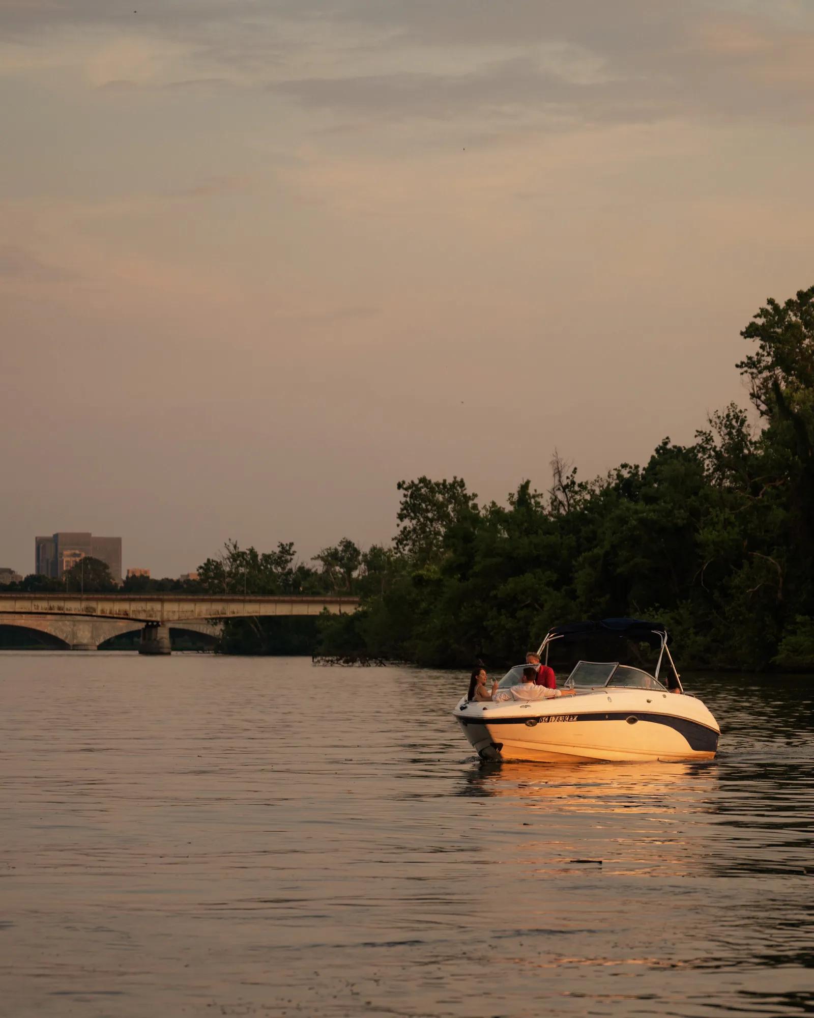 Boat cruising along the Potomac River with a bridge in the background at sunset and foliage