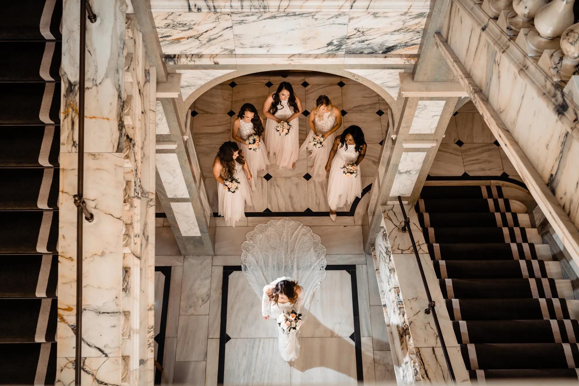 Bride descending marble staircase with bridesmaids at Rosewood London wedding venue in central London