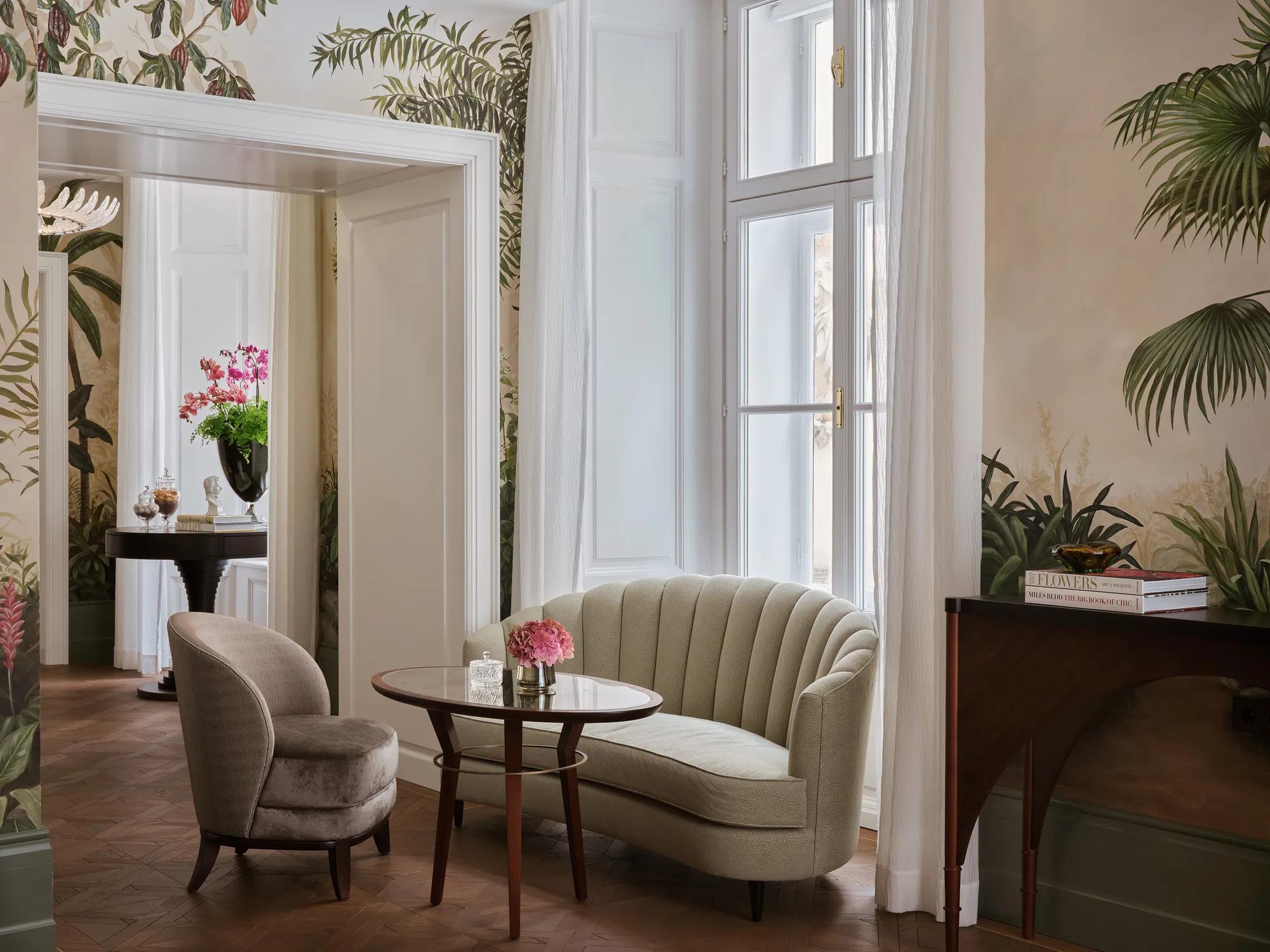 Salon Aurélie at Rosewood Vienna, featuring elegant seating with a mint-green settee, velvet chair, and hand-painted botanical wall murals in a refined, light-filled space.