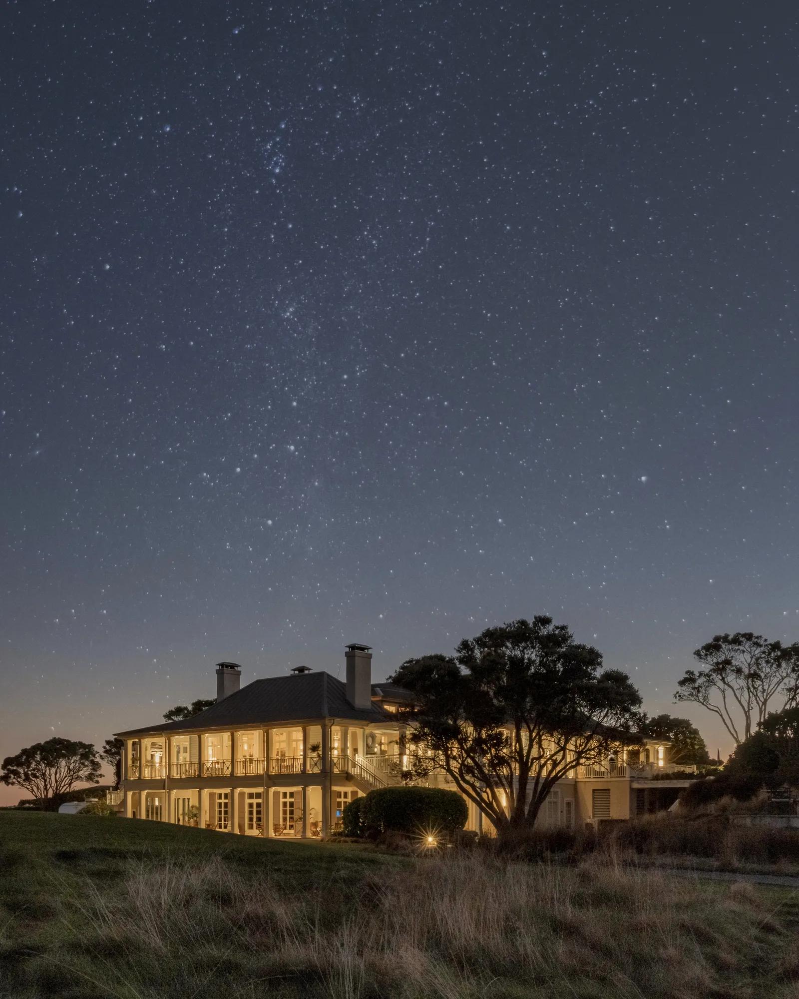 Night-time exterior of a luxury lodge in New Zealand with warmly lit interiors under the southern night sky.