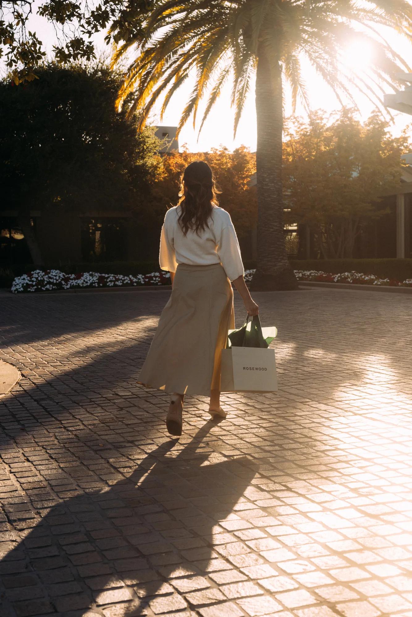 A woman carrying a holiday gift, walking toward the entrance of Rosewood Sand Hill.