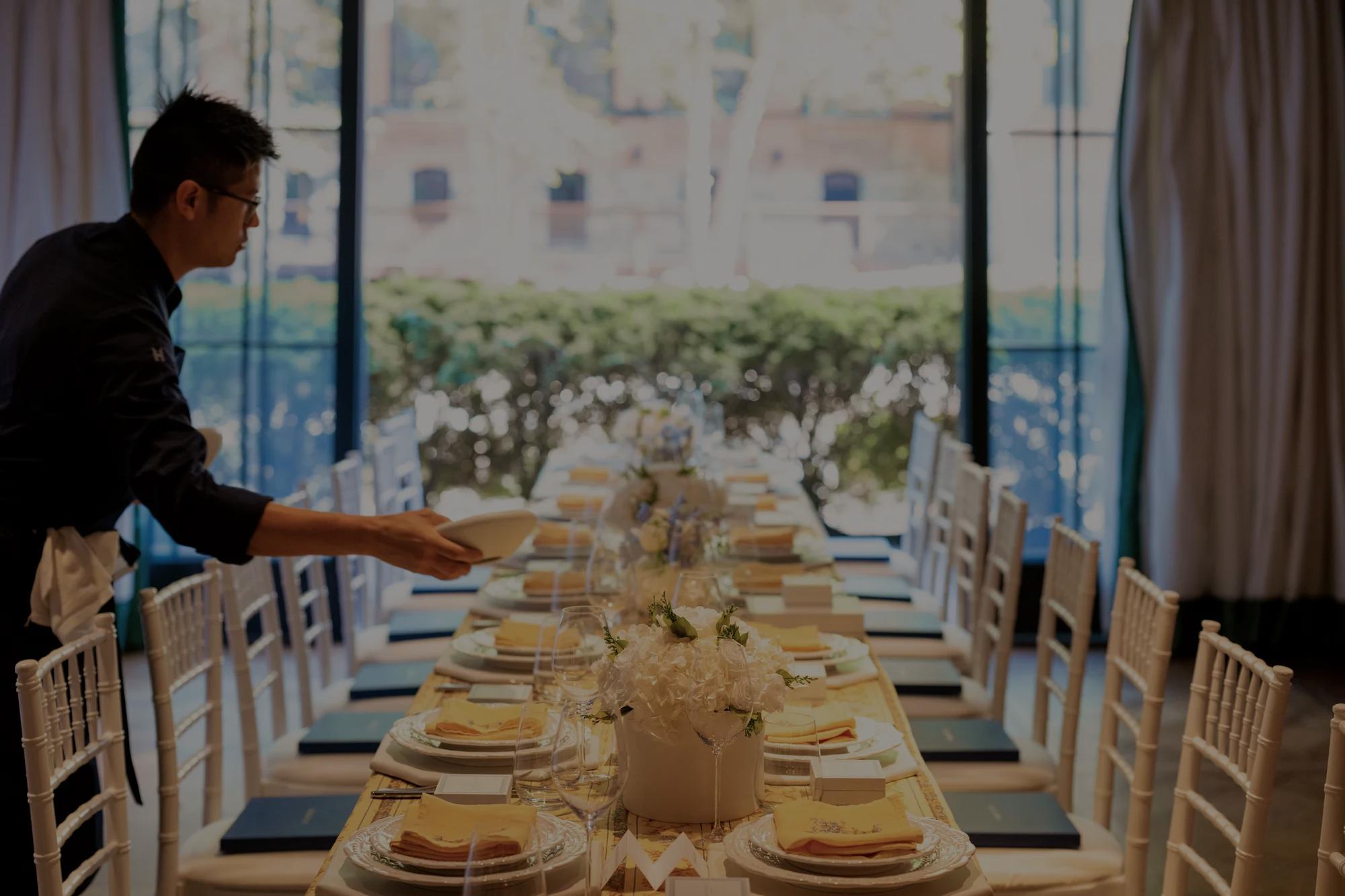 Event table at Rosewood Washington D.C. with final touches being done by a chef. Features yellow linen, white flowers, and white chairs.