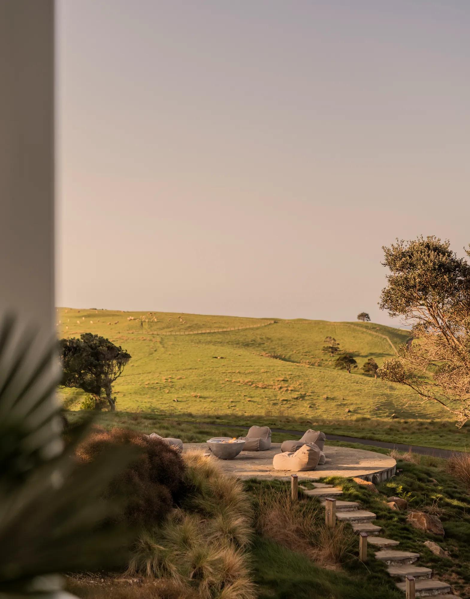 Sunset view of a cozy fire pit surrounded by seating, overlooking rolling green hills