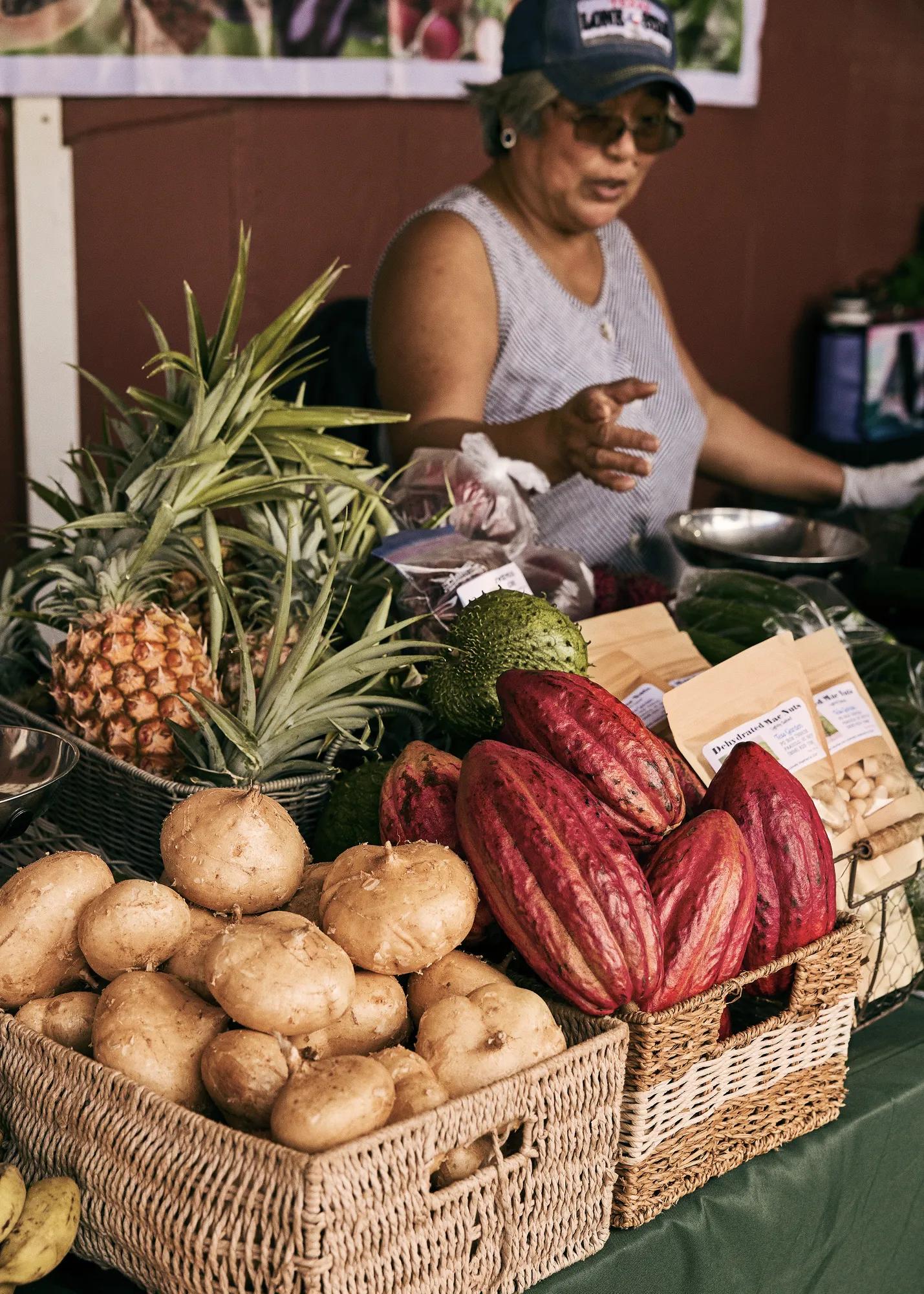 A purveyor at a farm stand with baskets of fresh fruit and a scale.