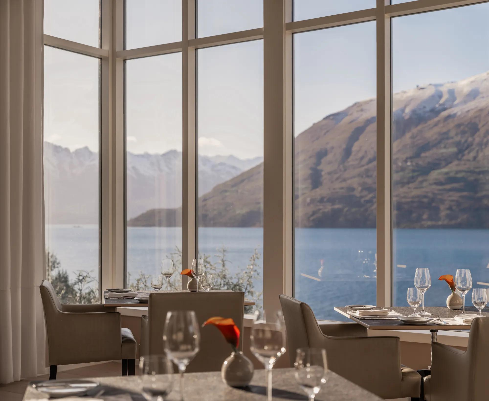 Dining room at Rosewood Matakauri with beautifully set tables and big picture windows to Lake Wakatipu and the snowcapped mountains.
