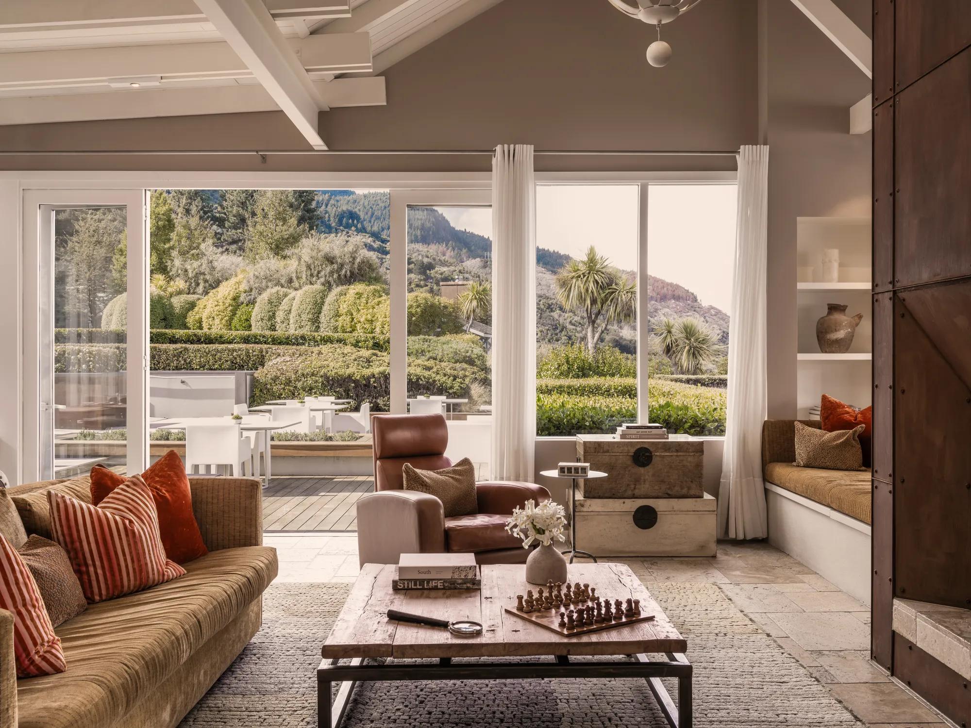 Lounge area at Rosewood Matakauri with luxury furnishings, Corten steel fire and open doors to a sunny terrace. 