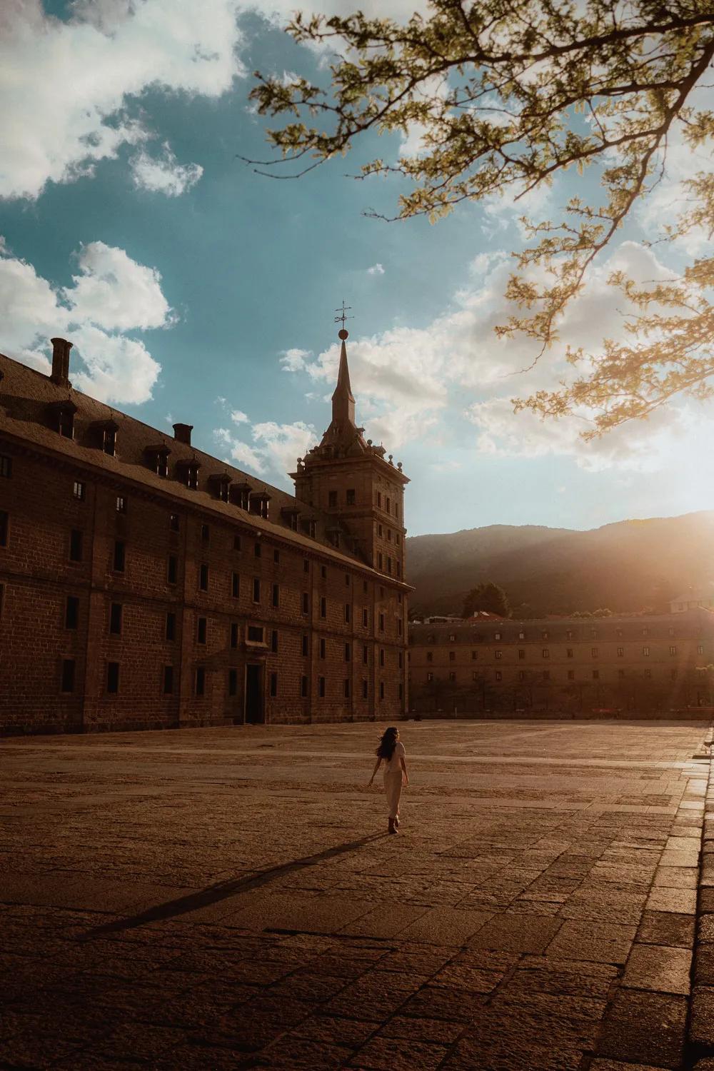 Cultural heritage site of El Escorial at sunset, with warm golden light illuminating the historic architecture, as a girl strolls peacefully through the grounds