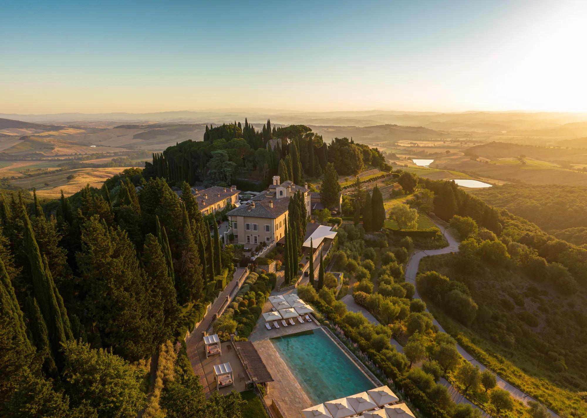 Pool at a luxury Tuscan resort, framed by cypress trees and landscaped gardens.