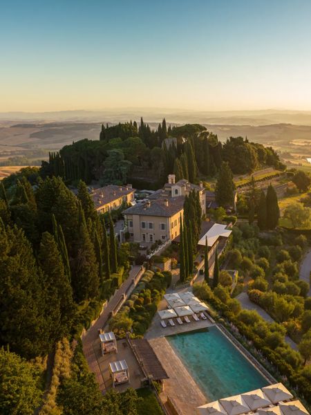 Piscina di un resort di lusso tra cipressi e giardini curati.