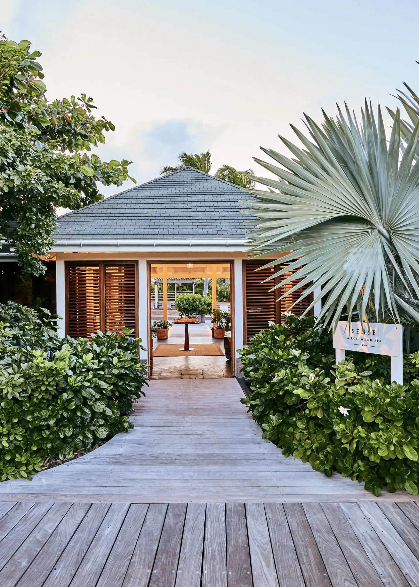 The outside of a luxury spa in St. Barths with wooden accents and greenery leading toward the property.