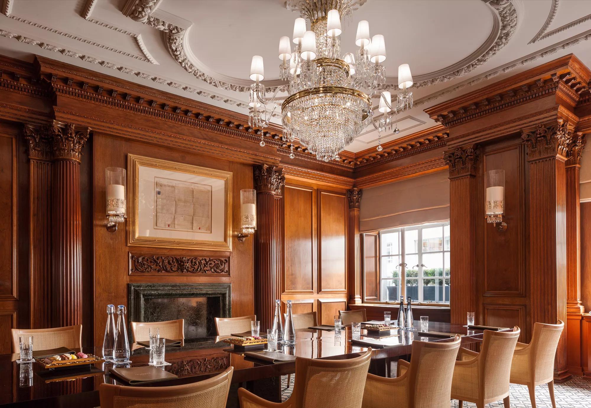 Elegant wood-paneled business meeting room at Rosewood London with a long conference table, crystal chandelier, fireplace, and natural light from tall windows.