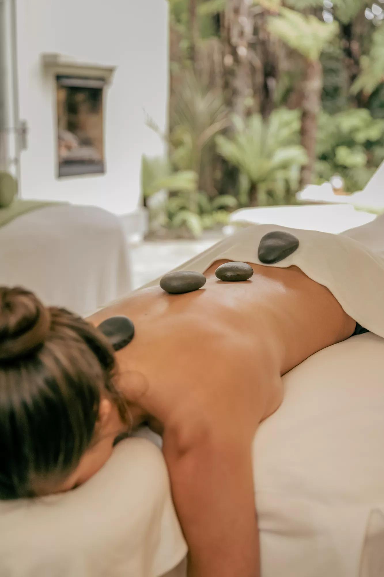 Woman relaxing on a massage bed in a private spa treatment room with volcanic hot stones placed along her back during a therapeutic spa treatment.