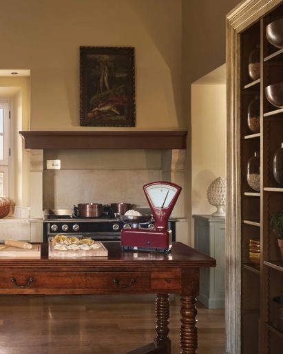 Una cucina con tavolo in legno, caminetto, fornelli e arredi tradizionali con opere d’arte.