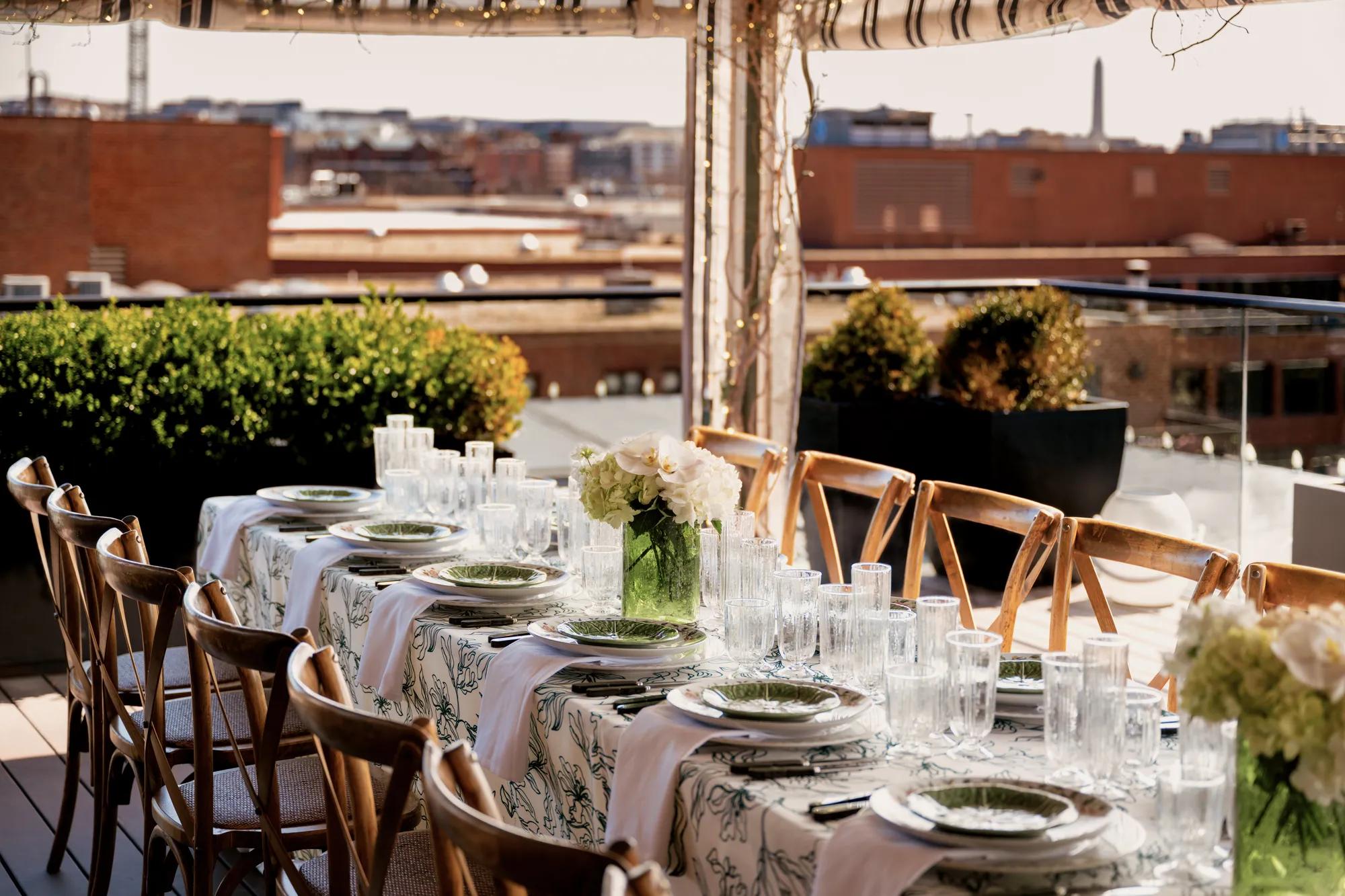 A long table set with brown wooden chairs and a patterned linen, featuring colorful flatware and plateware with the Washington Monument in view.