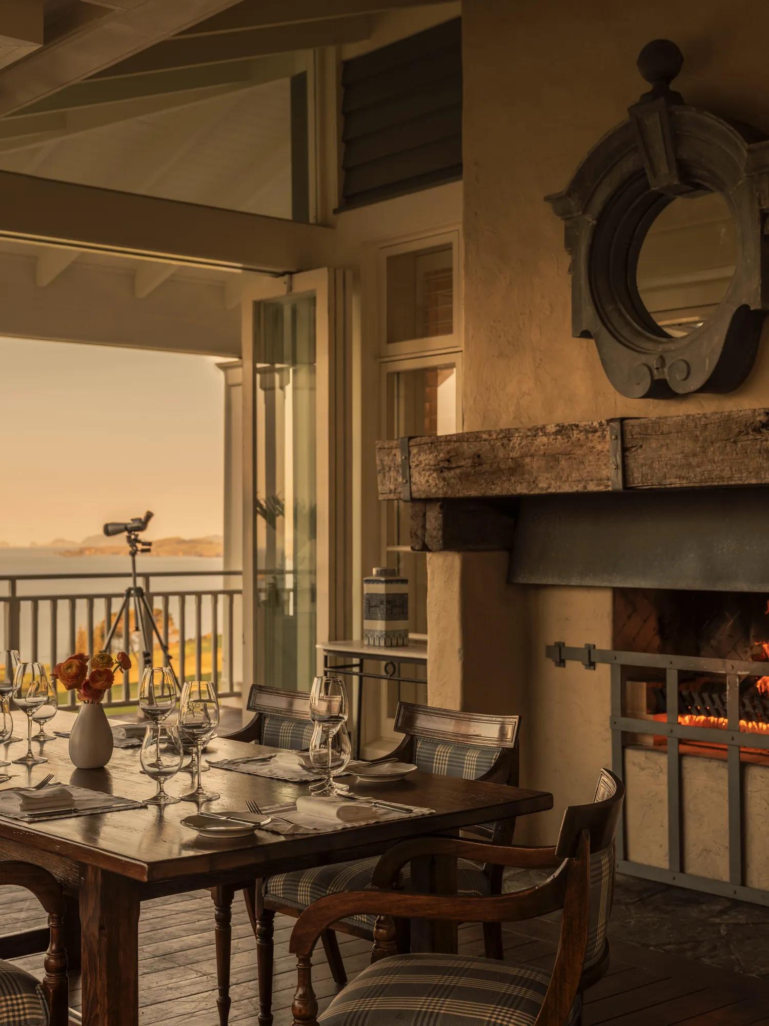 Private dining set up in a covered outdoor balcony with open fire and ocean views.