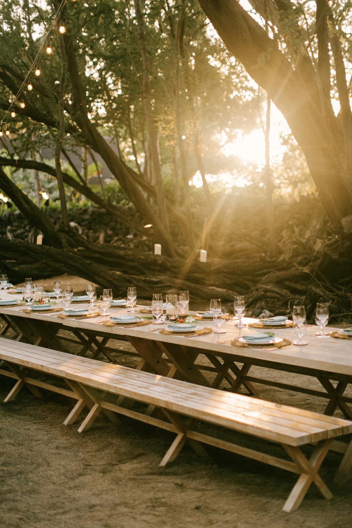 Long dinner table set with glass and plateware with sunset in background