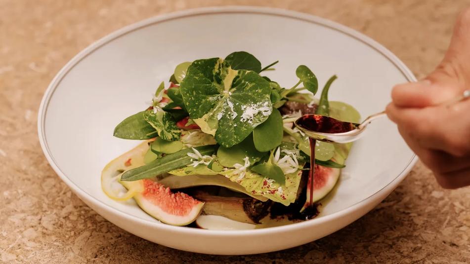 A man in a suit is pouring red wine from a  bottle into a glass.
