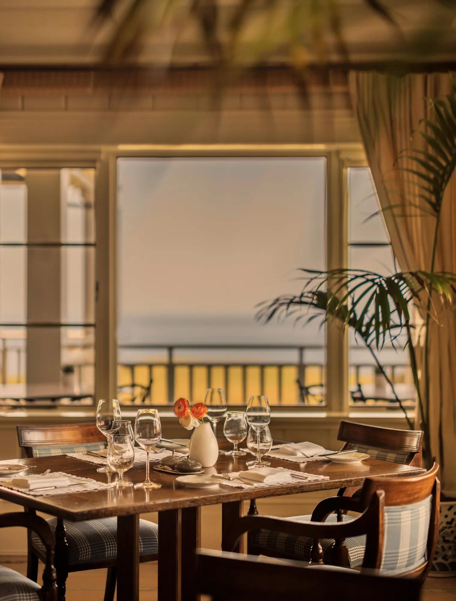 Set table in The Dining Room at Rosewood Kauri Cliffs looking out the big picture window to views of the golf course and ocean beyond.