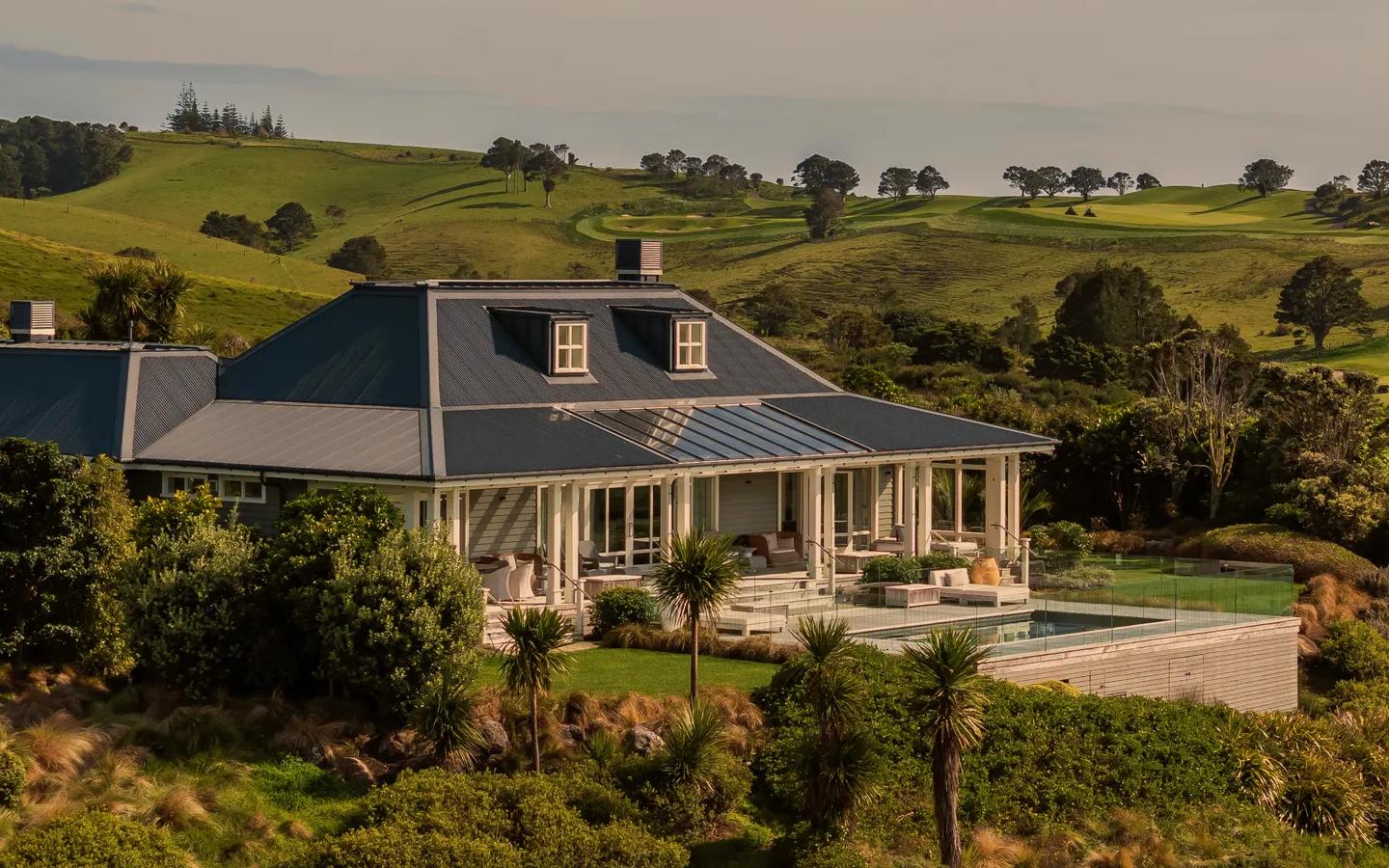 Front view of a luxury villa with an outdoor pool and spacious terrace, surrounded by a golf course and rolling green hills.