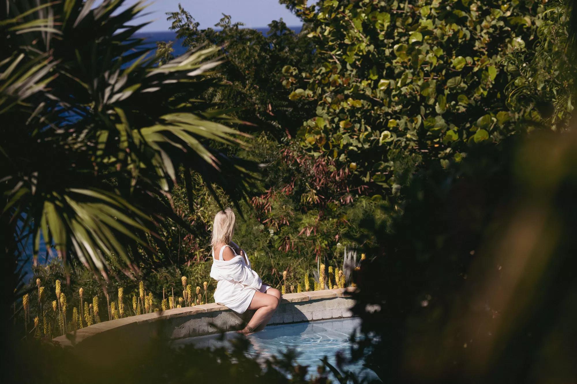 Outdoor pool with stone tile walls surrounded by palm trees and tropical gardens.