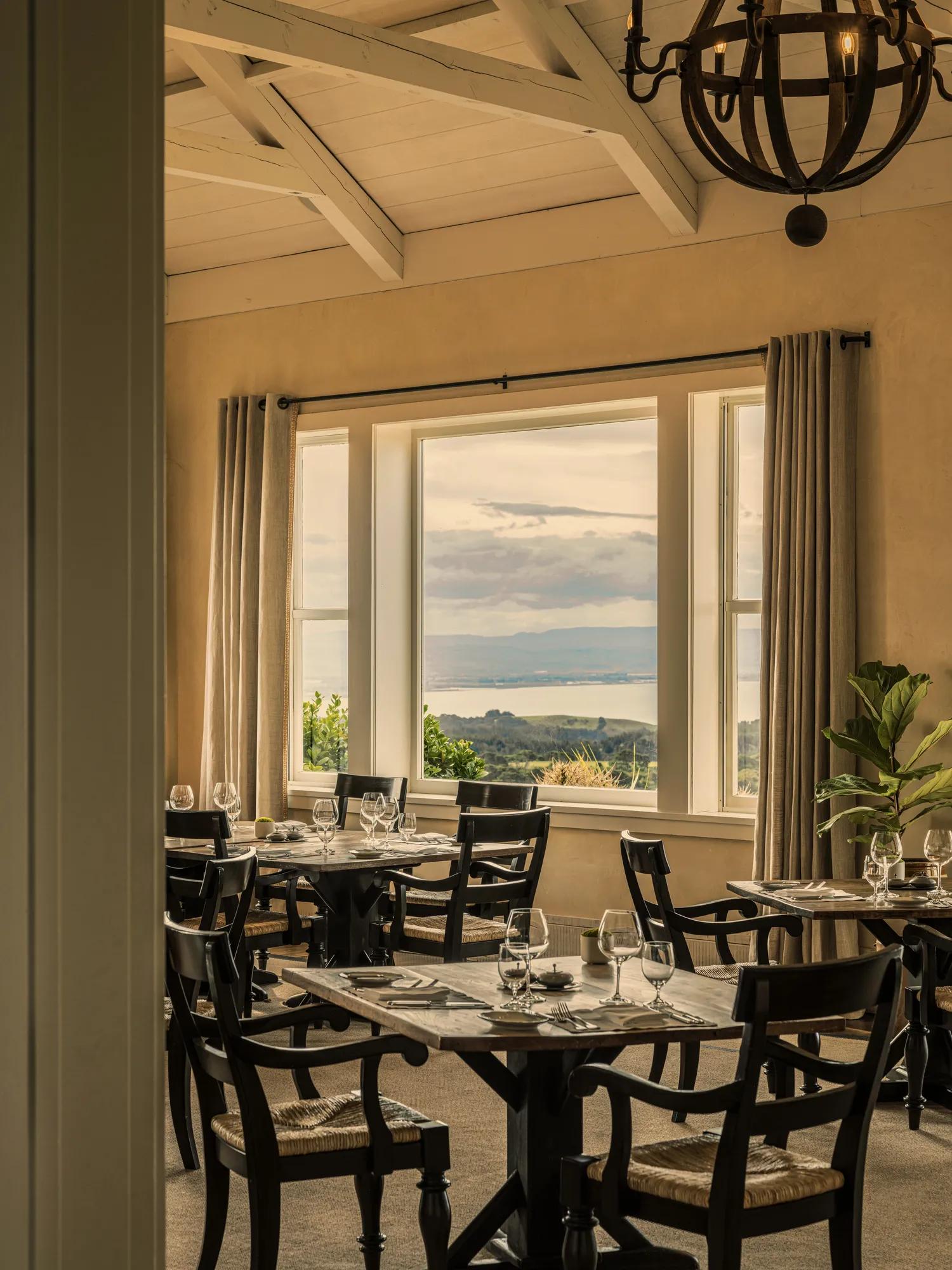 Looking through to the Main Dining Room at Rosewood Cape Kidnappers, with beautifully set tables and views out the window to the Hawke's Bay.