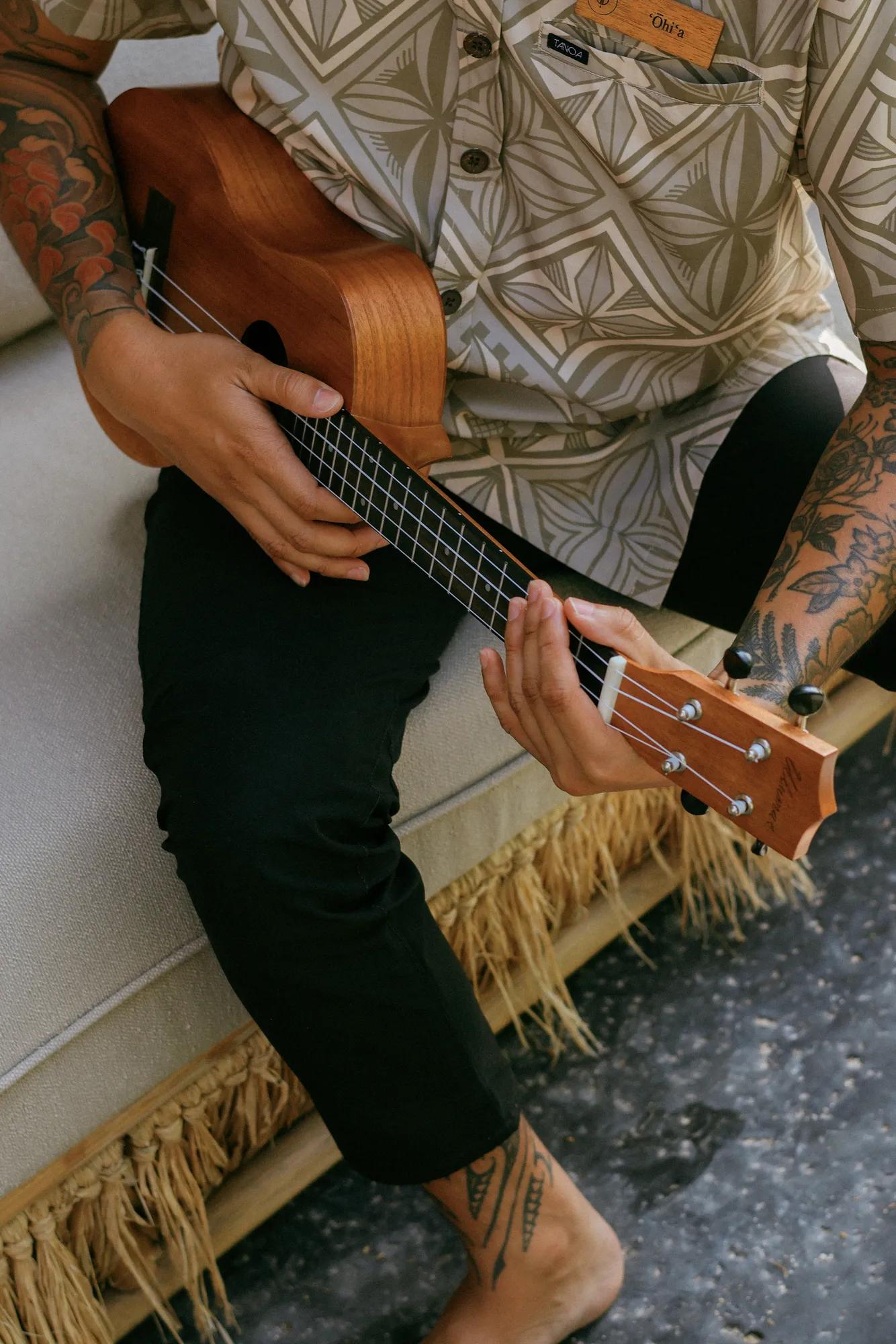 Close up shot of tattoed arms playing wooden ukulele