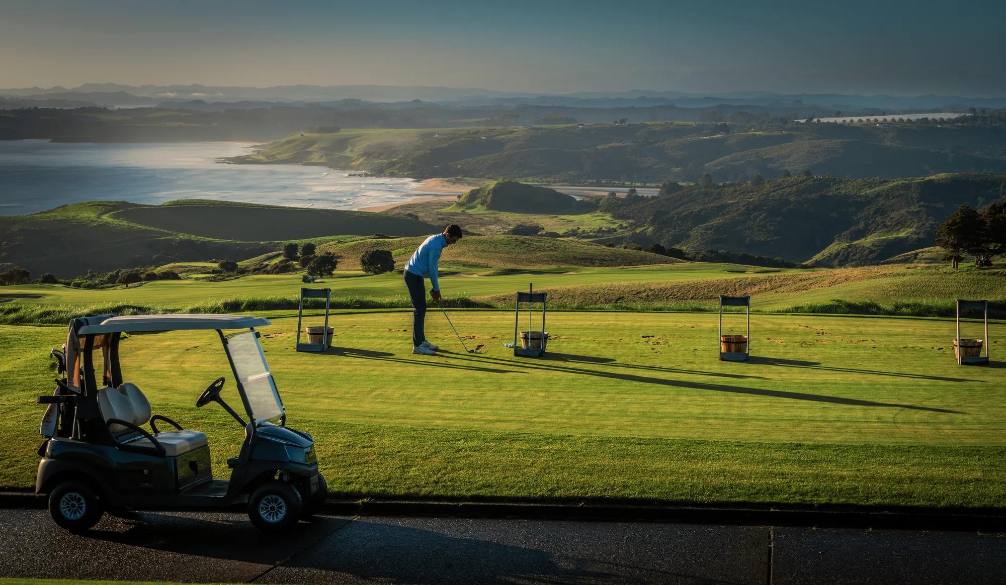 A man on an outdoor driving range with a vast view out to the coastline and ocean.