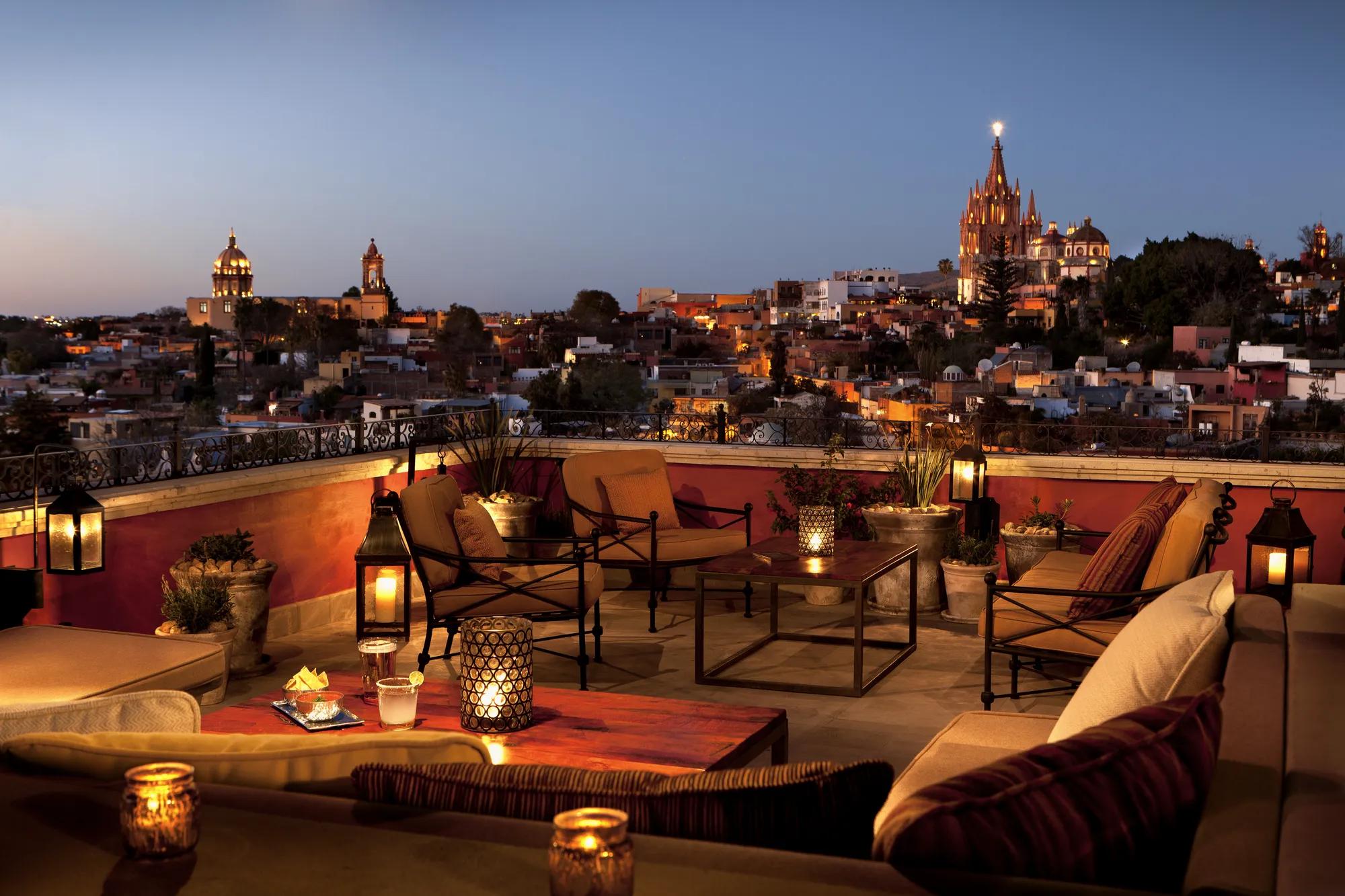 Luna Rooftop terrace with cozy seating overlooking the Parroquia at dusk, capturing the warm glow of evening lights and the city skyline.