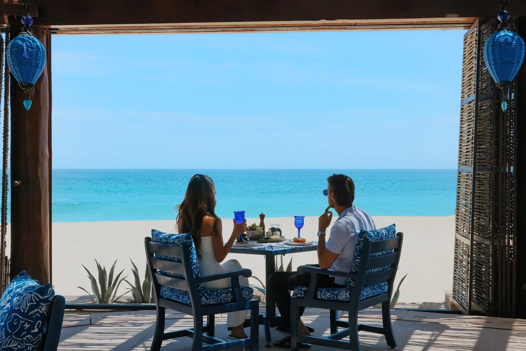 Couple enjoying an outdoor beachfront dining experience with blue ocean views and clear skies