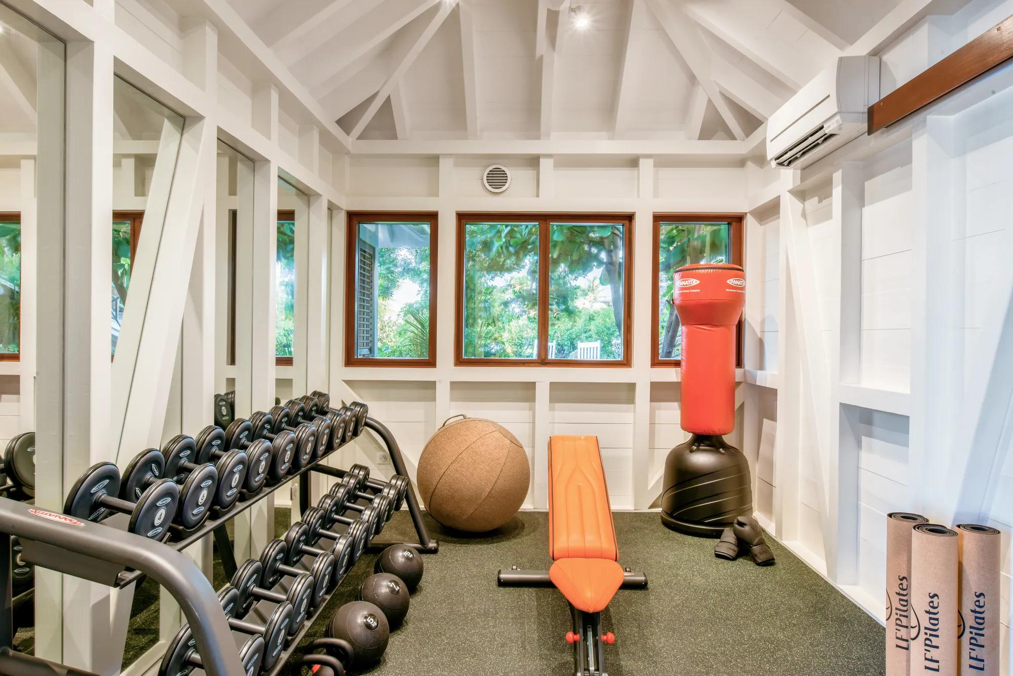 Hotel fitness centre with weights and cardiovascular machines, mirror wall on the right and windows at the end that looks out to the indoor pool.  