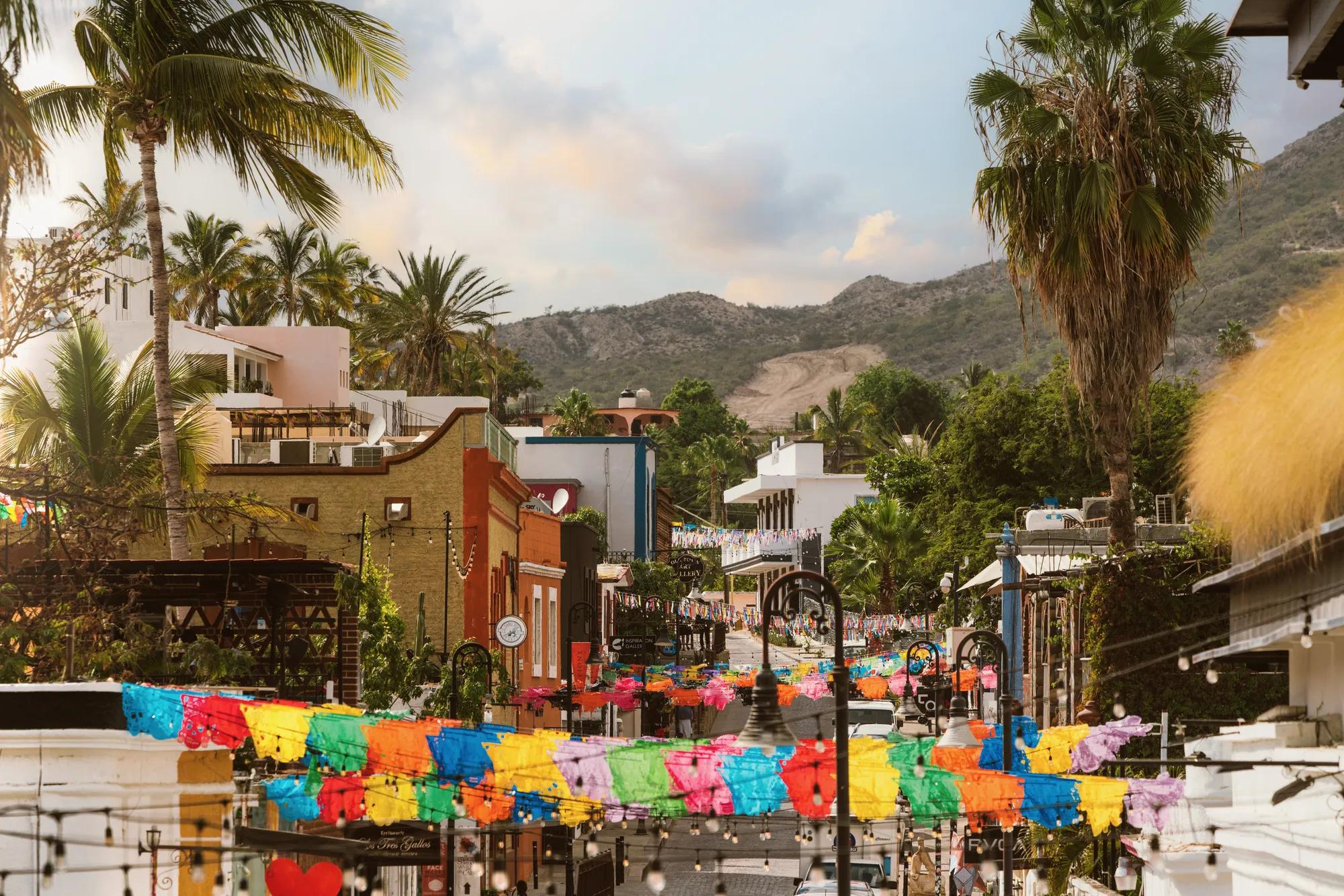 A colorful cobblestone street in San José del Cabo, Mexico, with Spanish colonial buildings, palm trees, and festive banners overhead