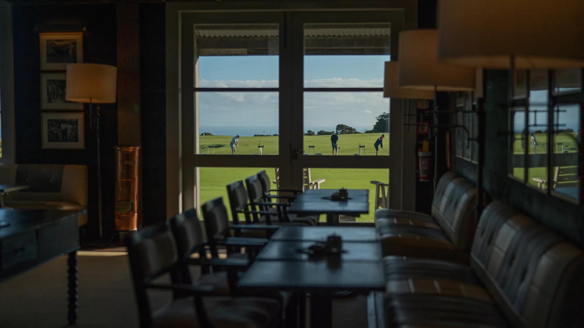 Dining set up in the Cape Kidnappers Golf Course Club House, out the window three golfers are practicing their shots.
