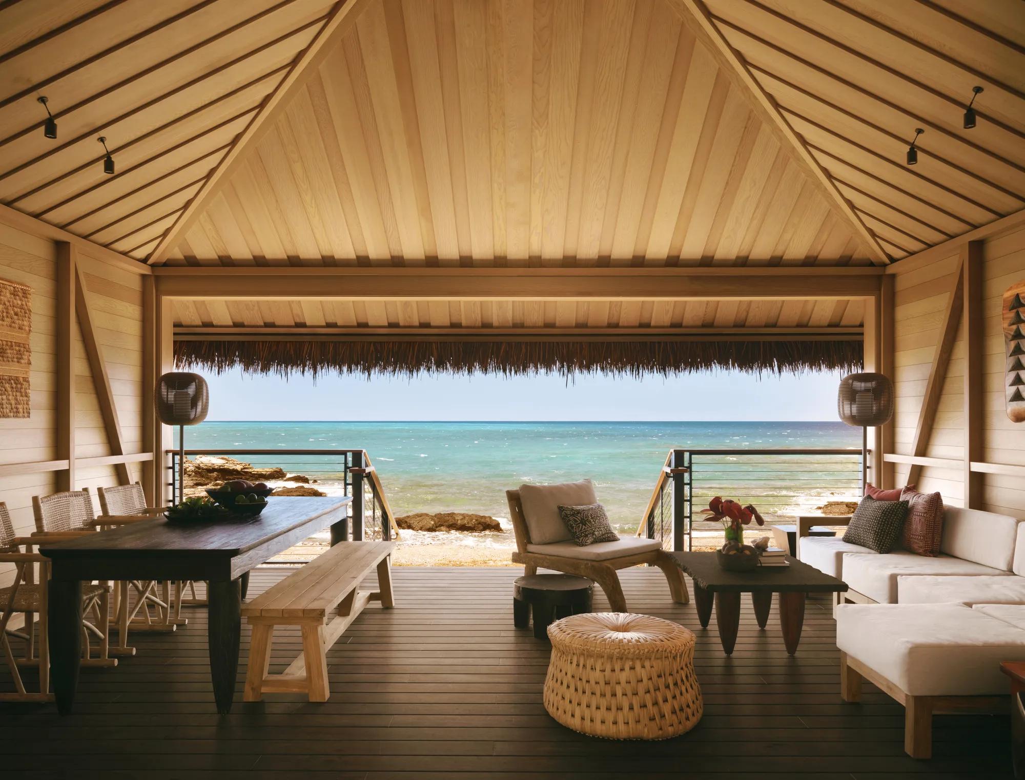 Ocean view from a four bedroom suite overlooking the horizon with palms along the shoreline and poolside loungers next to the infinity pool of the space