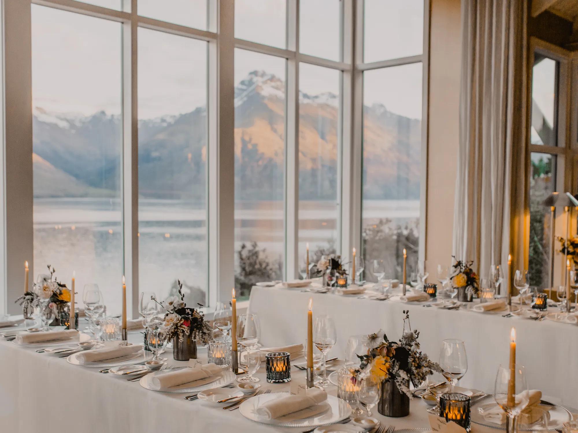 A view of a dining room with multiple tables set up to face the stiking view over a lake and mountain ranges. 