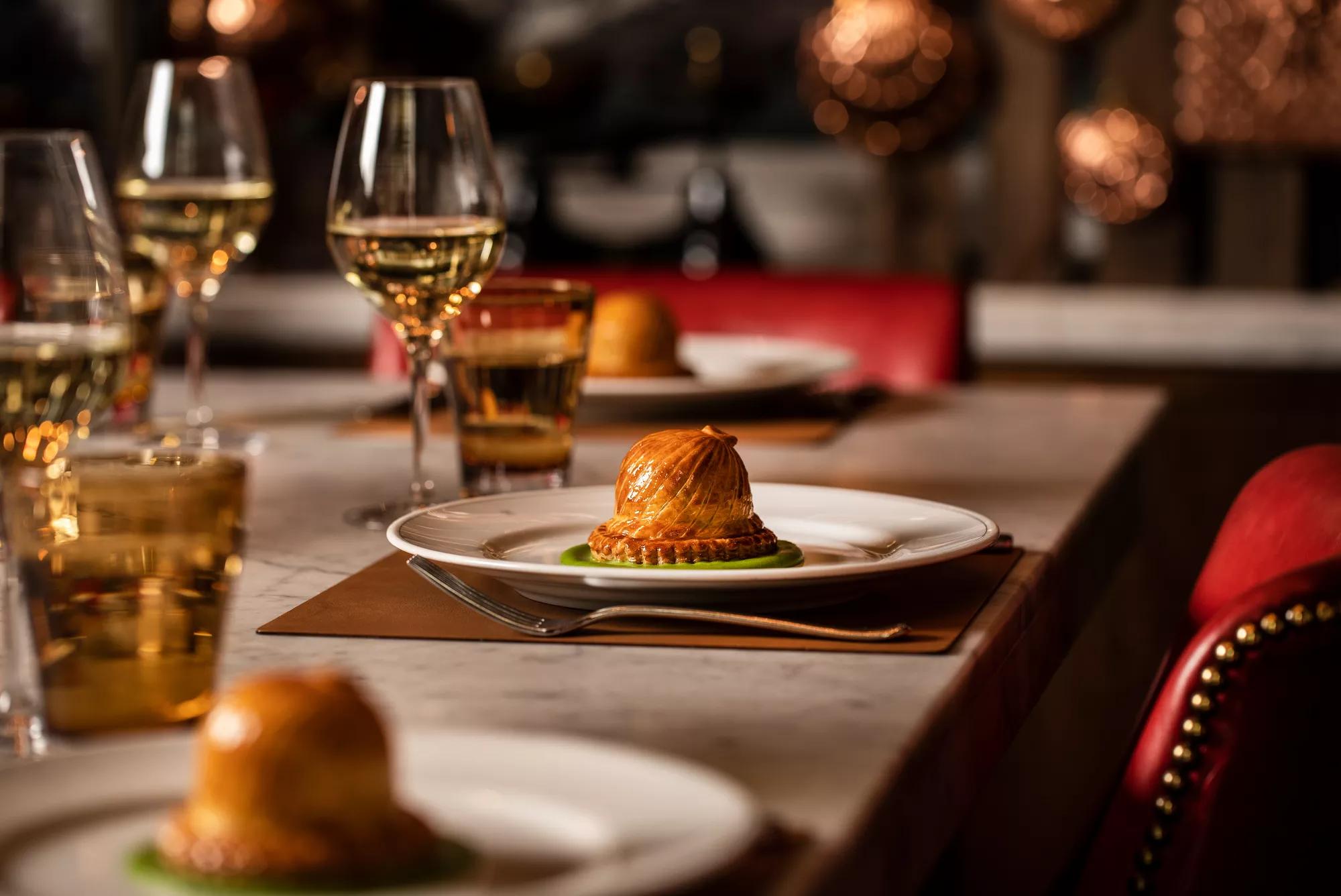 Modern British pie plated on a marble table with wine and warm lighting in a refined London restaurant.